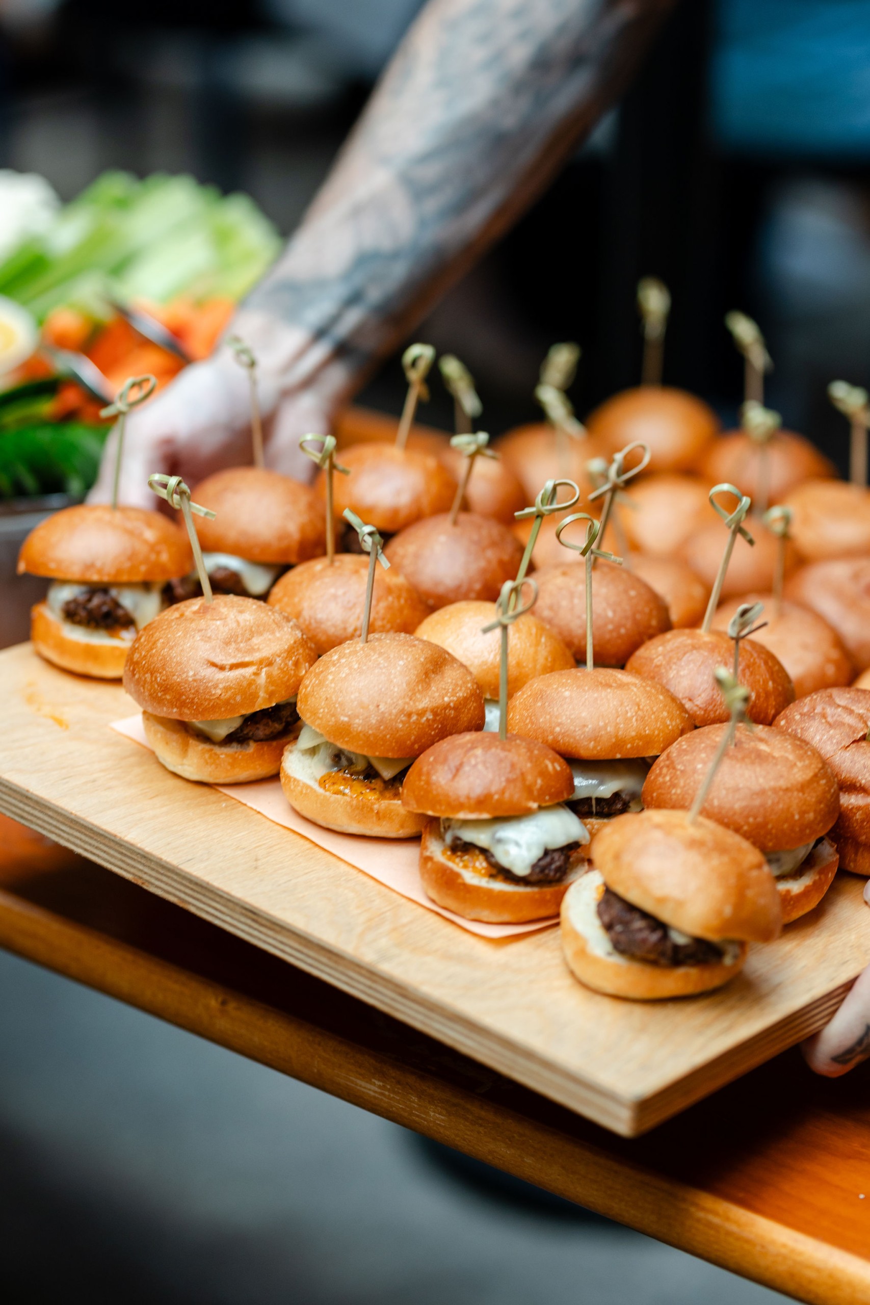 At a social event, a man captures moments of guests holding trays of sliders.