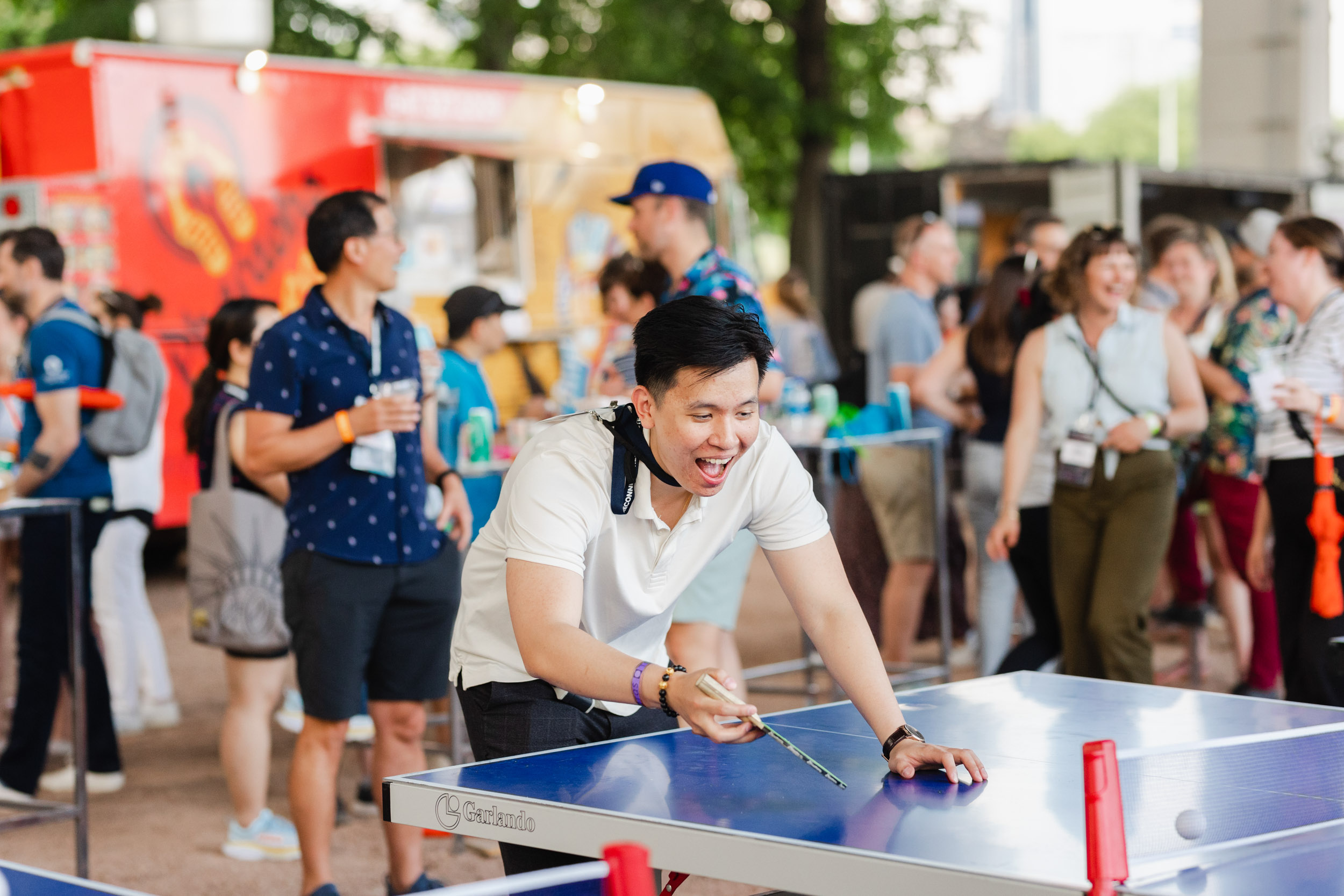 Photographer capturing a man playing ping pong at an outdoor conference event.