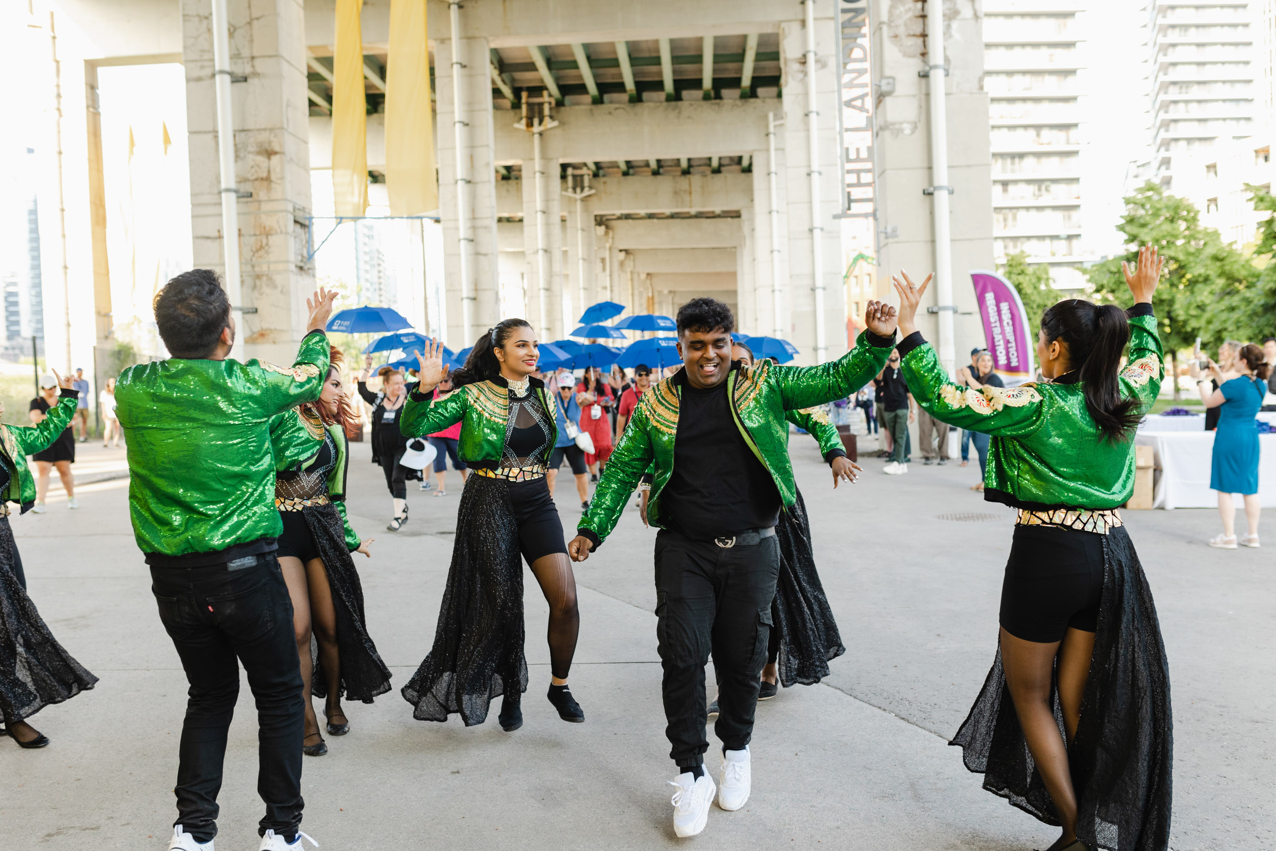 Conference photography: A troupe of dancers in green jackets performing on a bridge.
