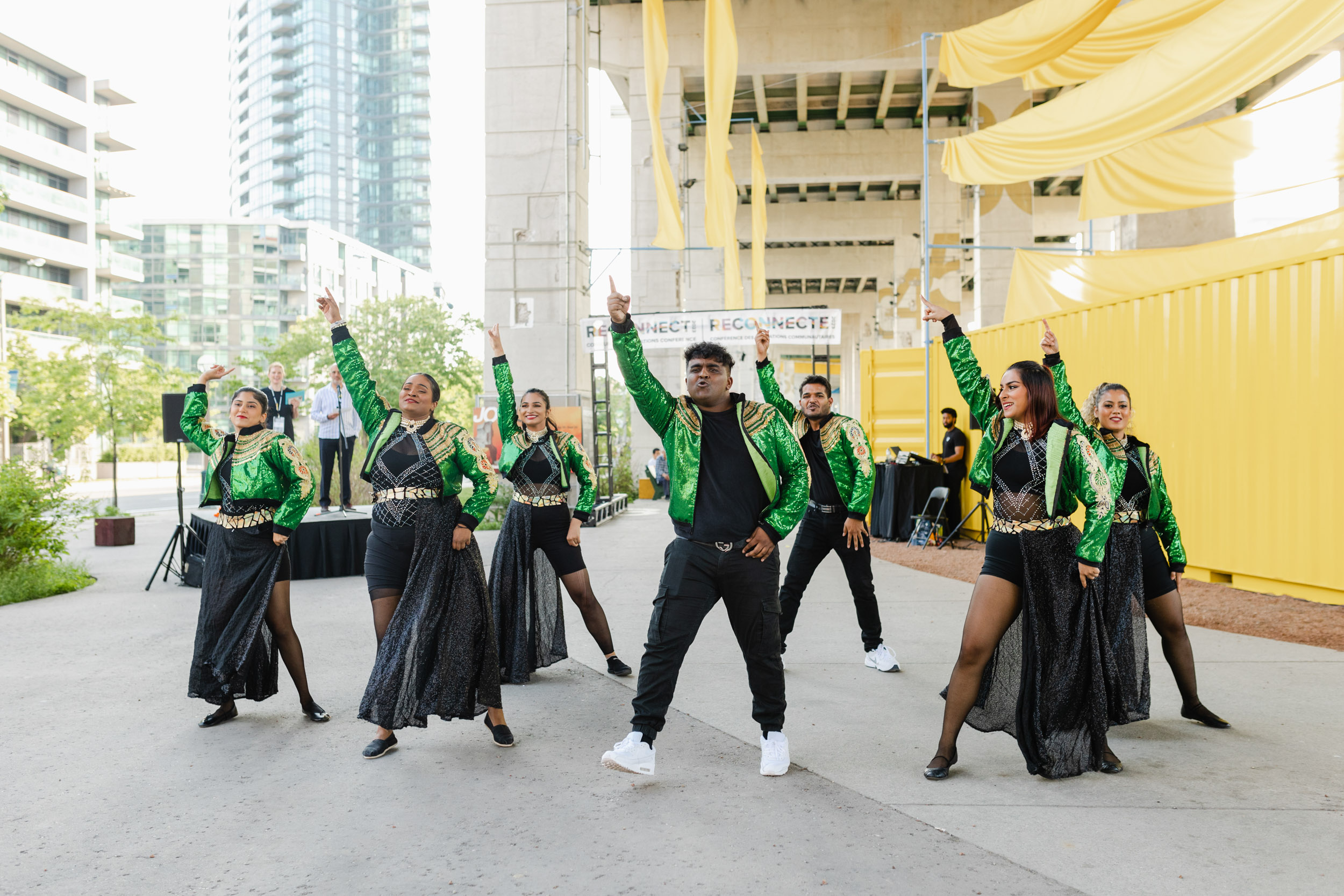 A group of dancers in green jackets standing outside a yellow building at a conference.