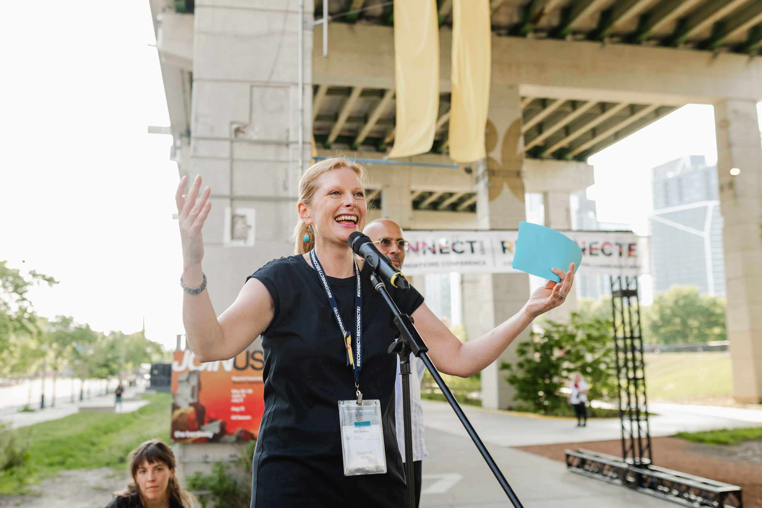 A woman is speaking at a conference in front of a bridge.