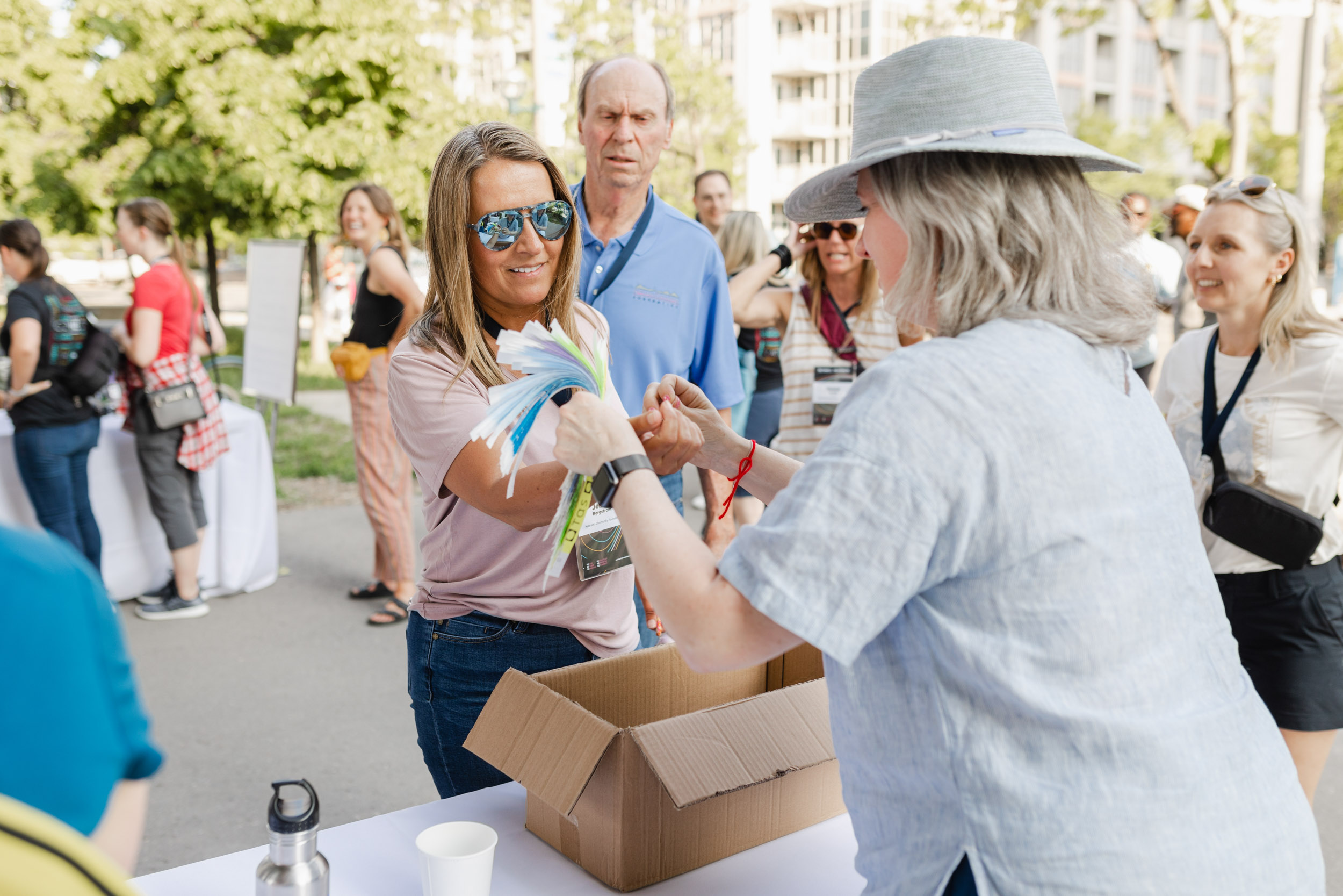 Conference Photography: Woman giving a box to another woman during an outdoor event.