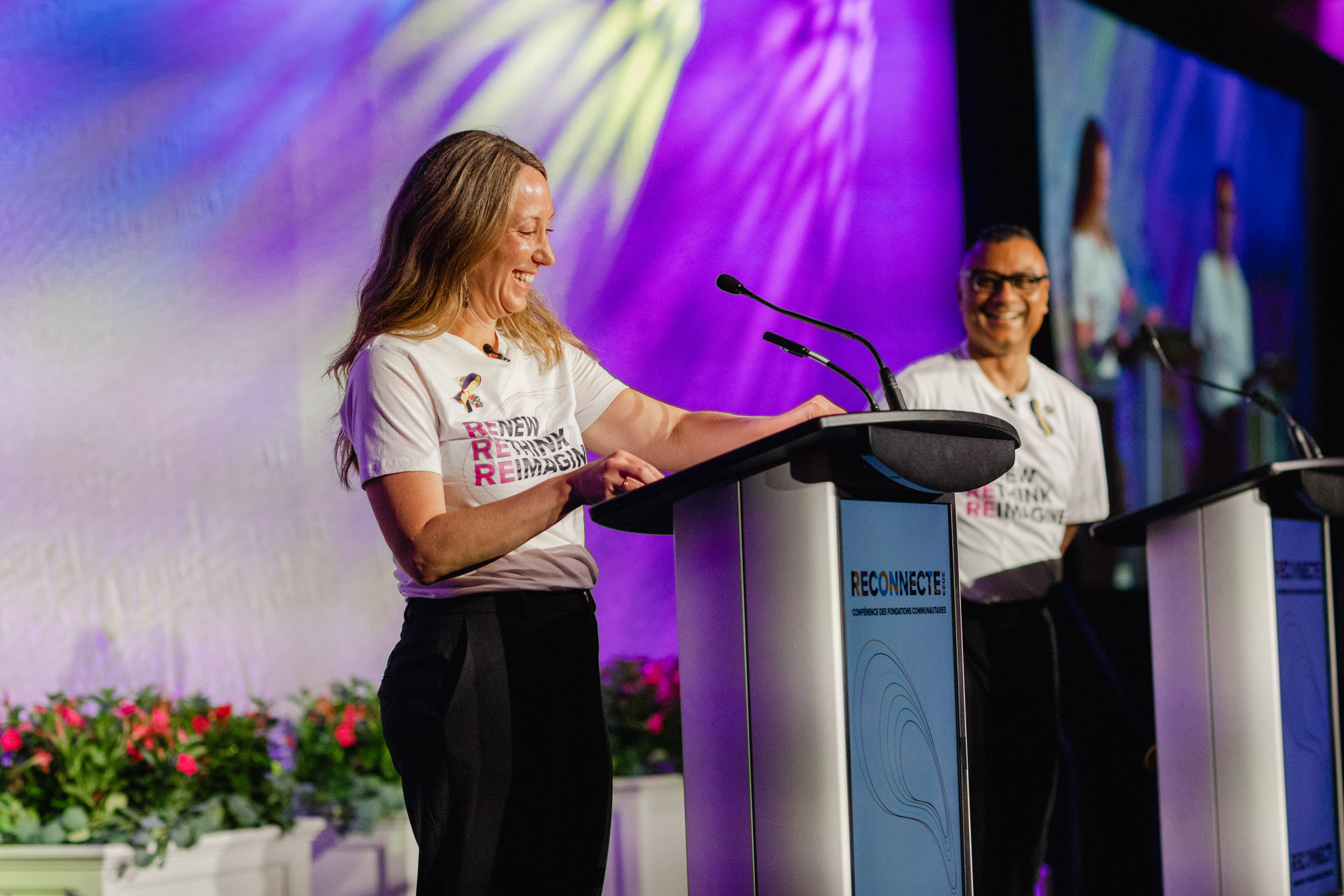 Conference photography of two women standing at podiums in front of a stage.