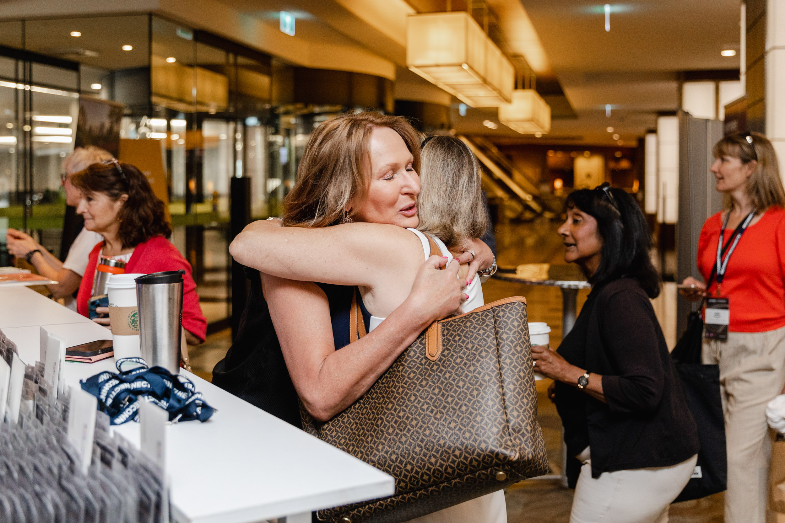 Conference photography: Two women embrace in a lobby.