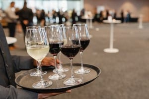 A man holding a tray of wine glasses at a grand opening event while being captured in photography.
