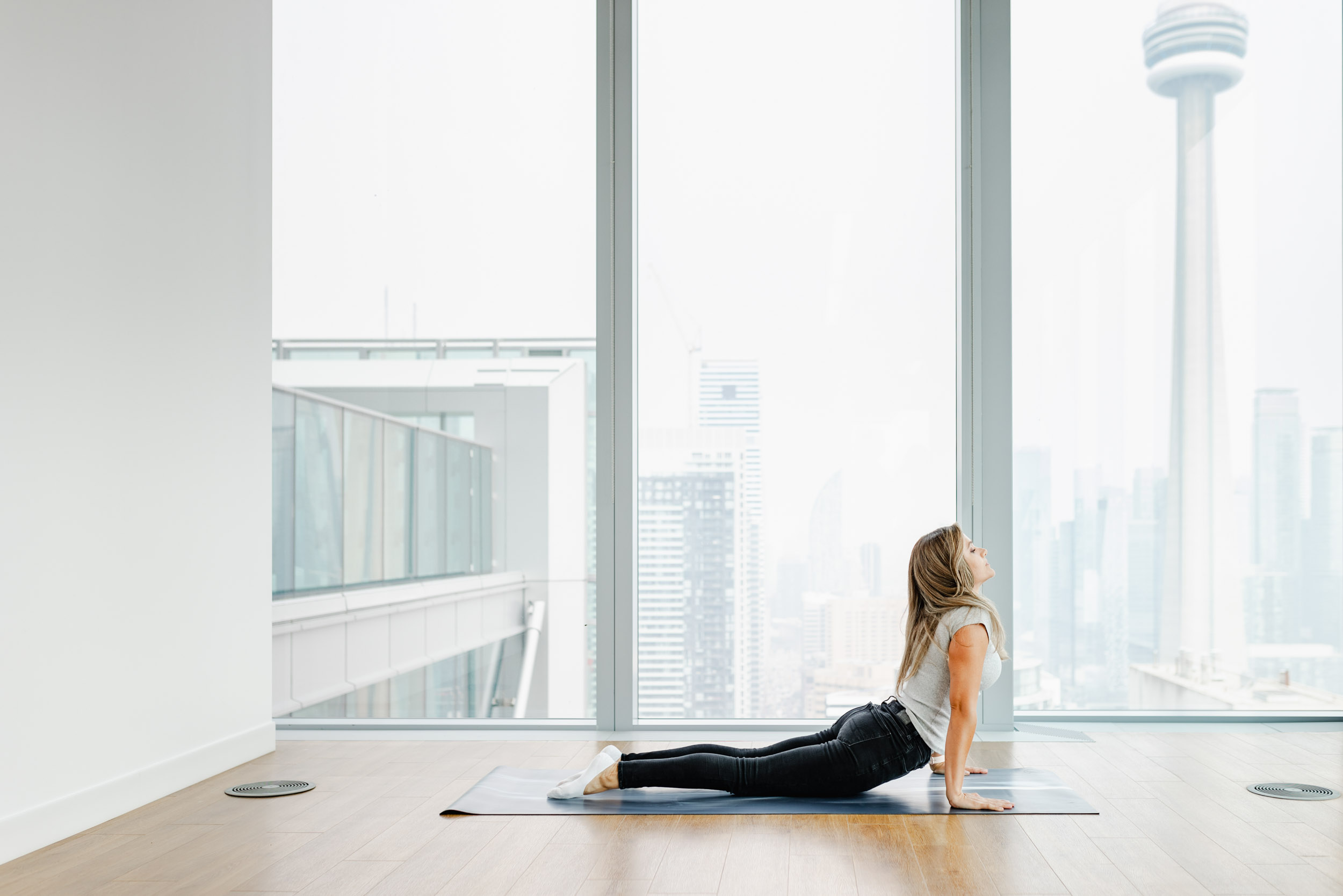 A woman practicing yoga in front of a large window, overlooking the city.