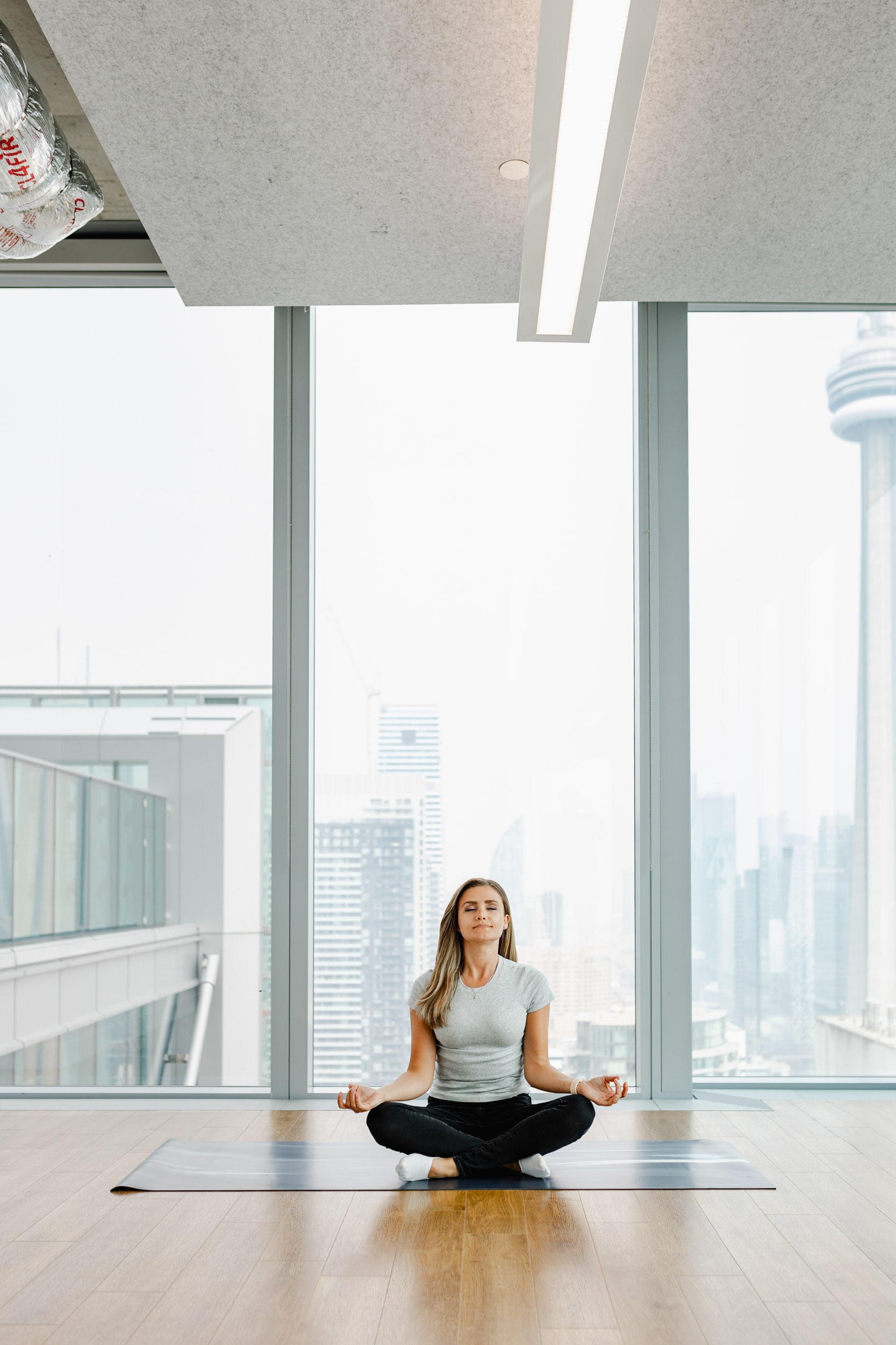 A woman is sitting on a yoga mat in a room with a view of the CN Tower, surrounded by advertisements from Index Exchange.