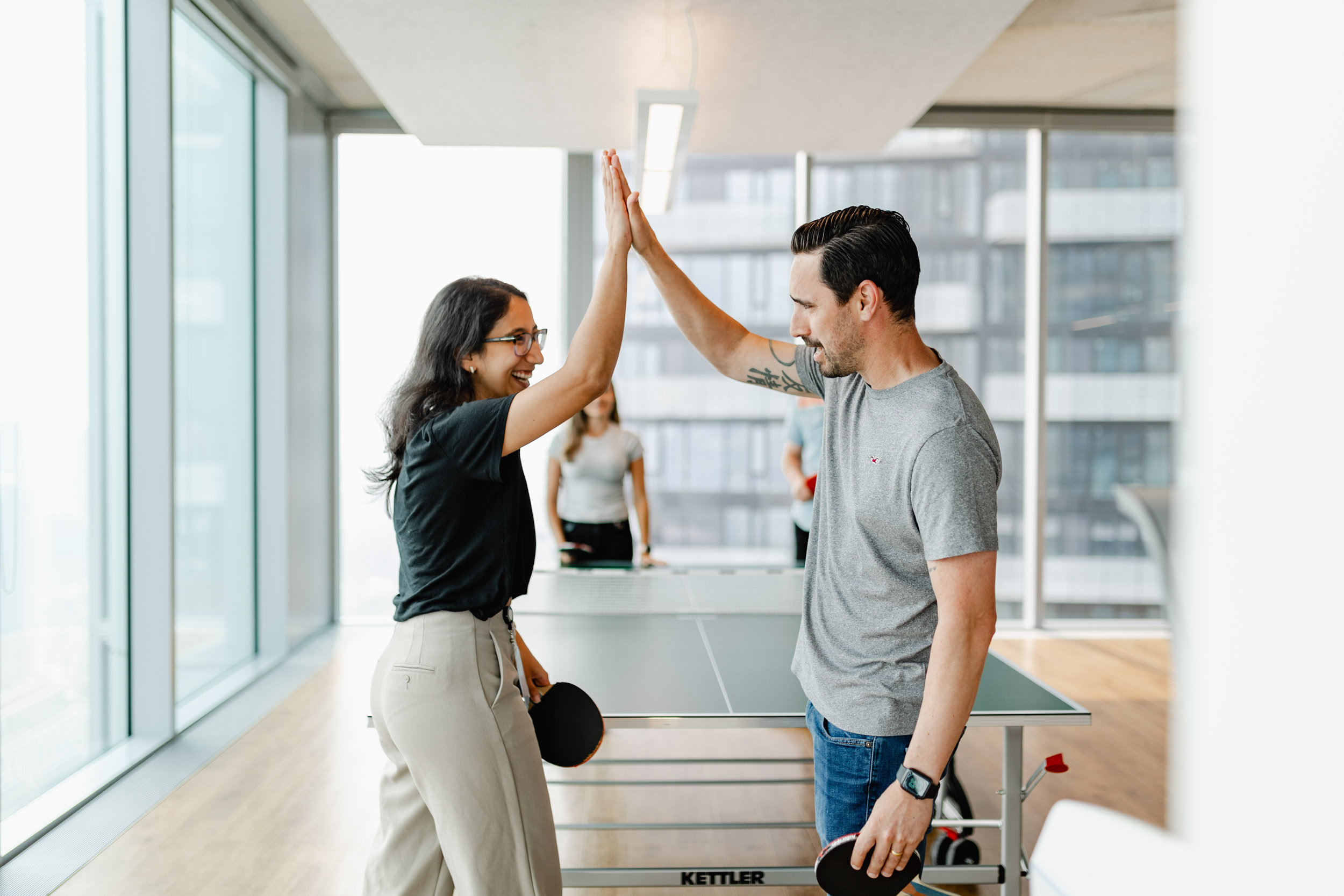 Two individuals engaged in a lively game of ping pong within an office space.