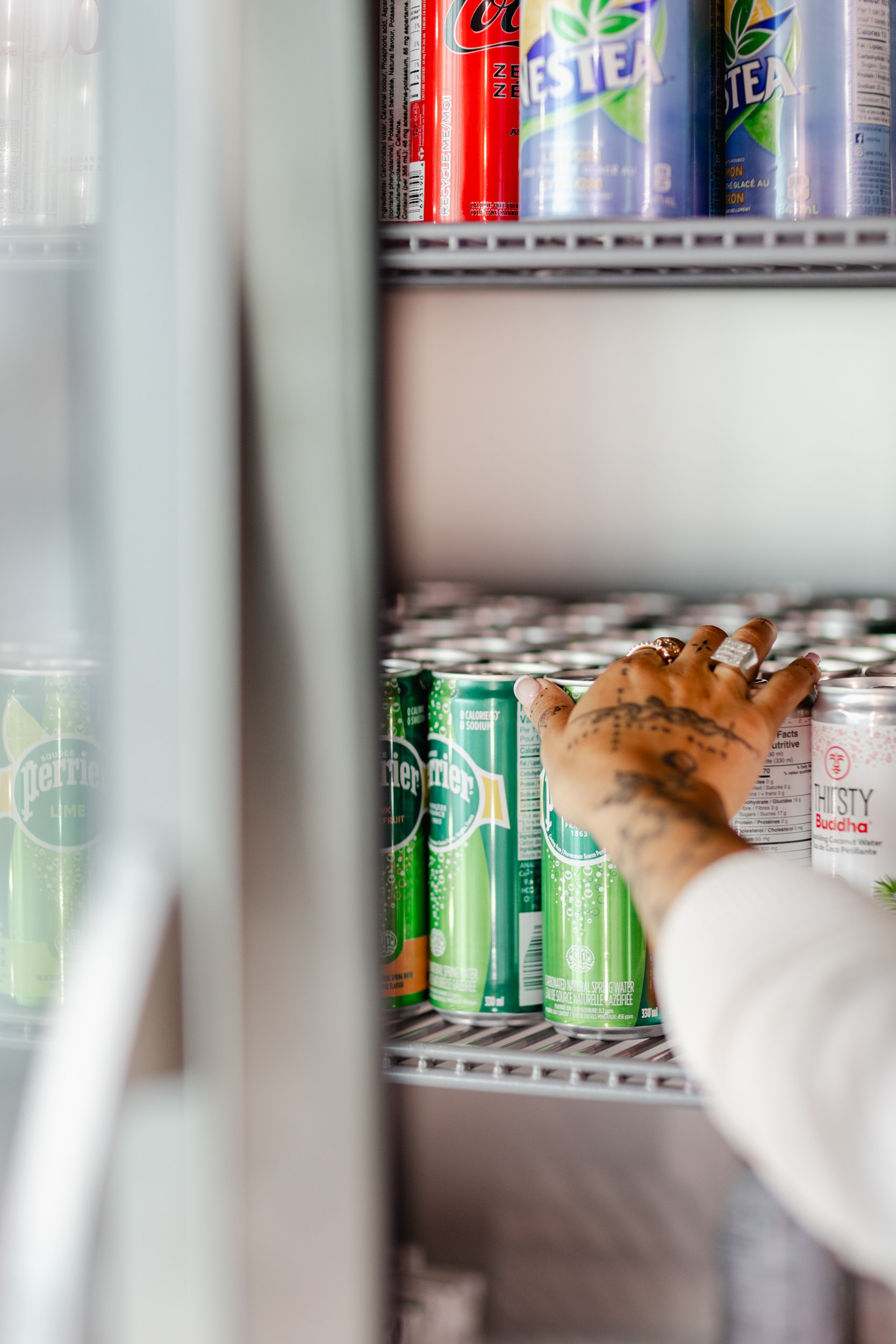 A hand reaching into an Index Exchange refrigerator full of cans.
