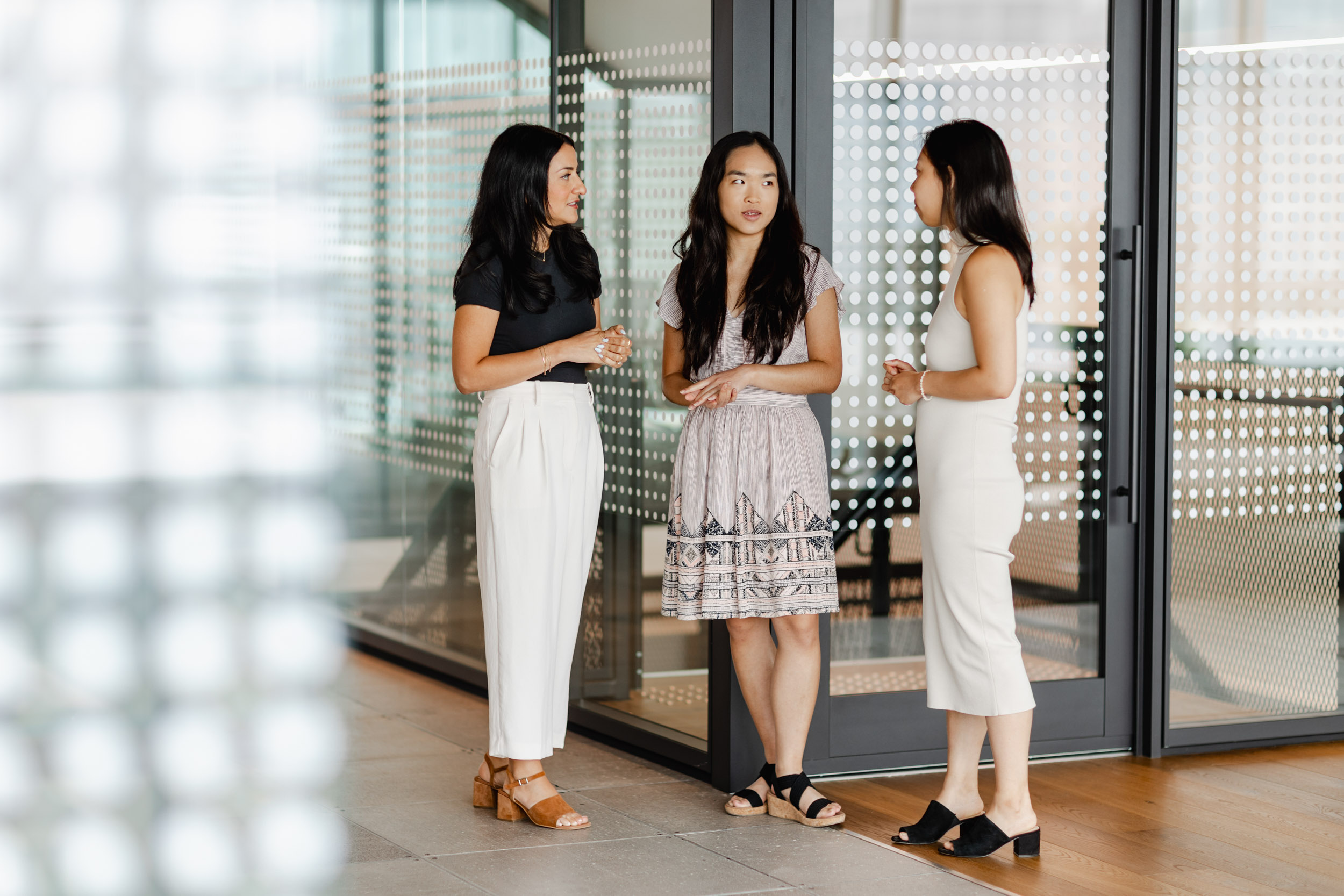 Three asian women discussing Index Exchange in front of a glass door.