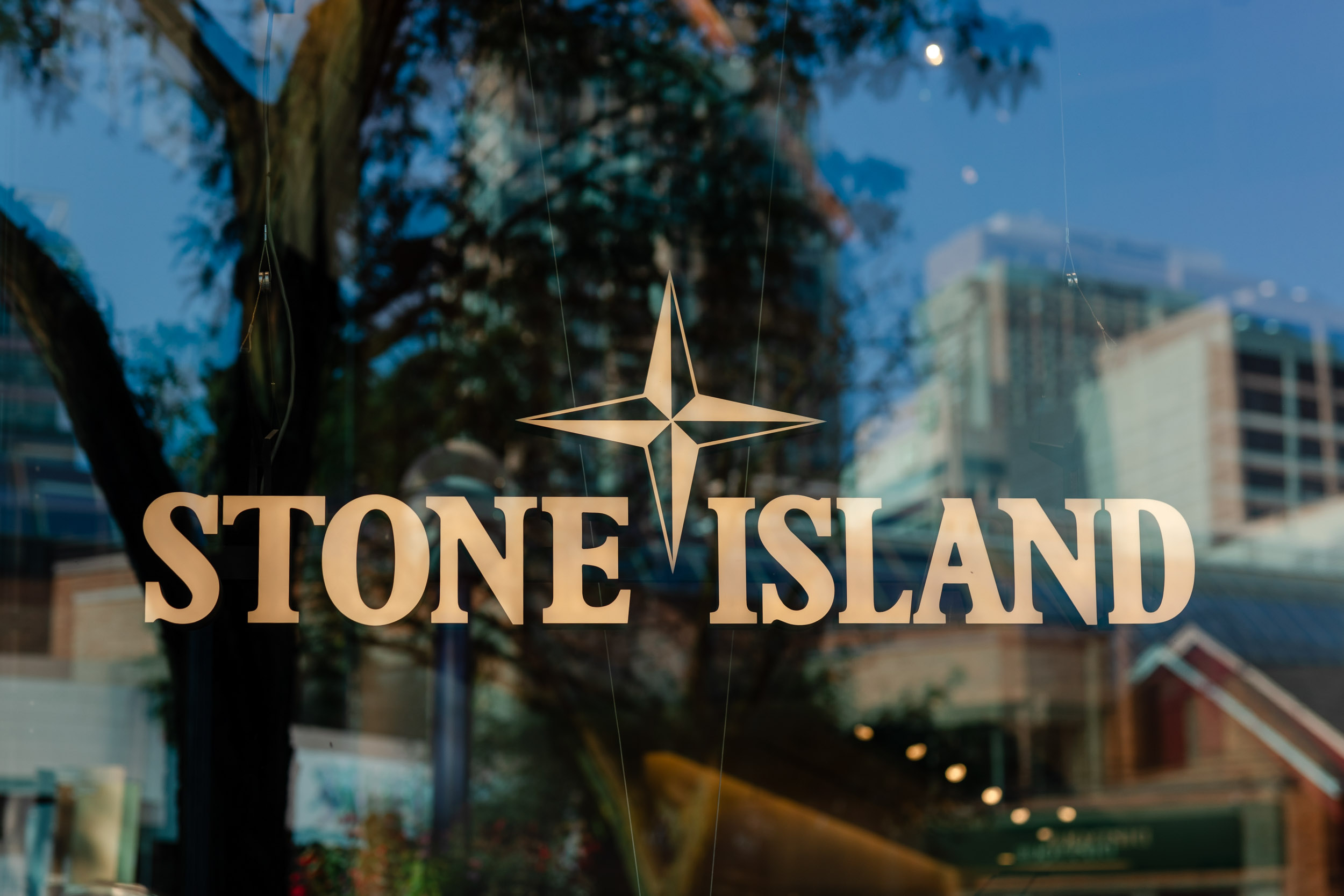 The Stone Island logo is reflected in the glass of a building.