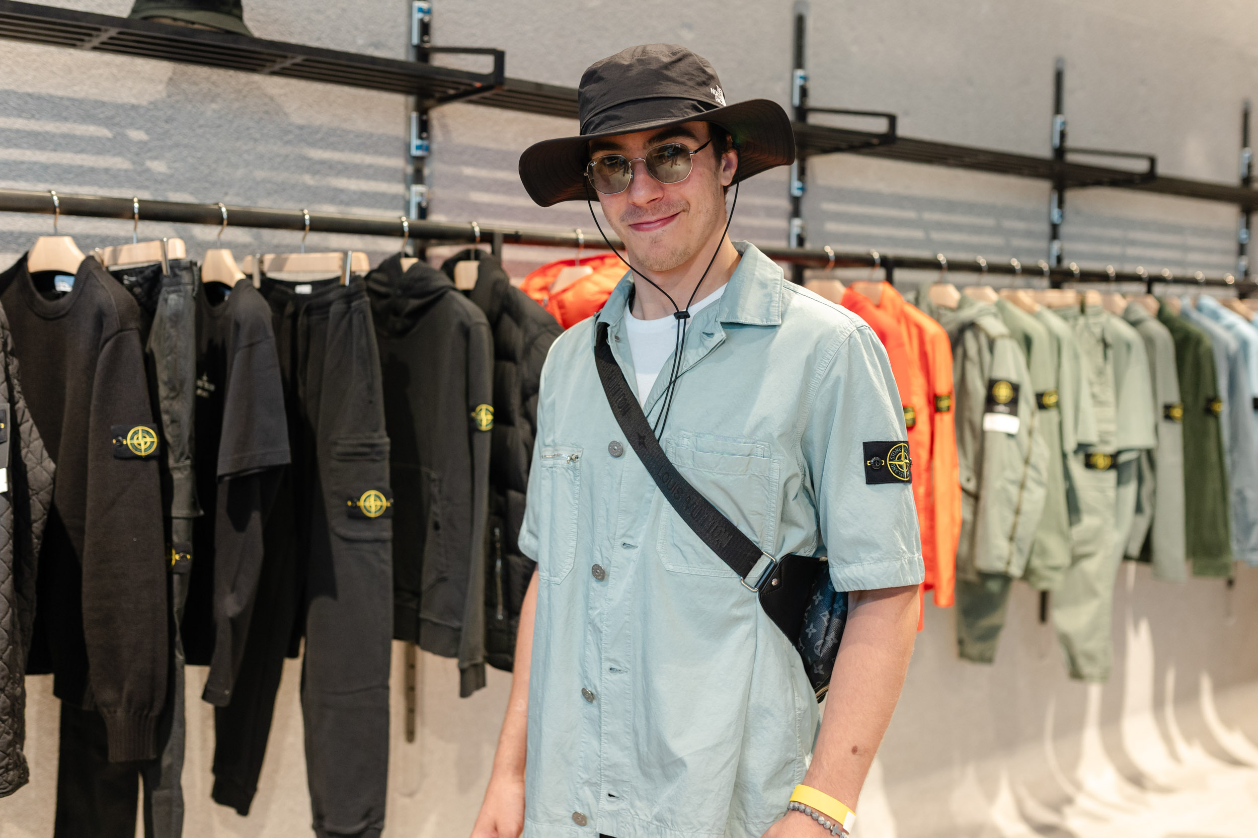 A man wearing a hat standing in front of a rack of clothes.