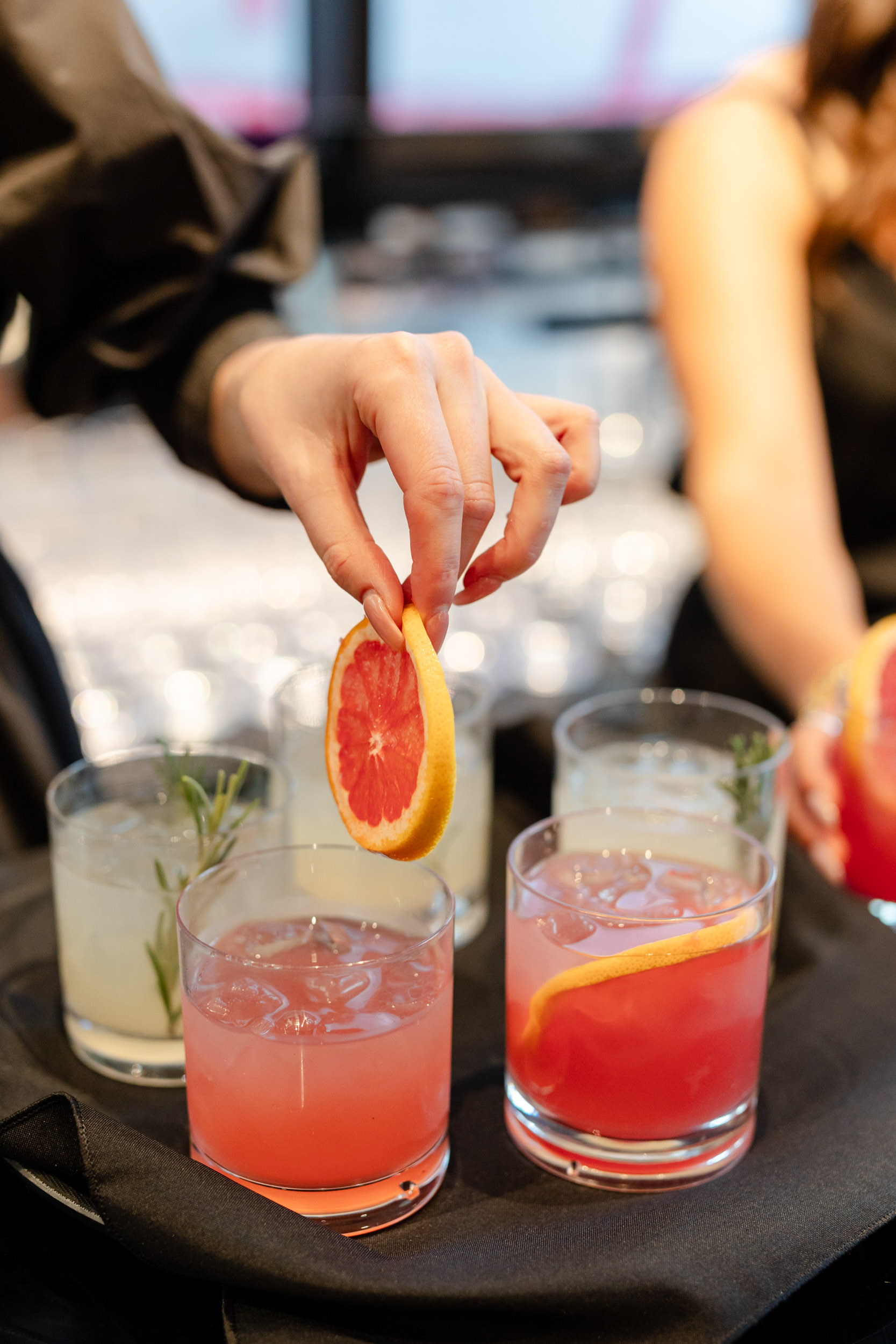 A woman is putting a slice of grapefruit into a glass
