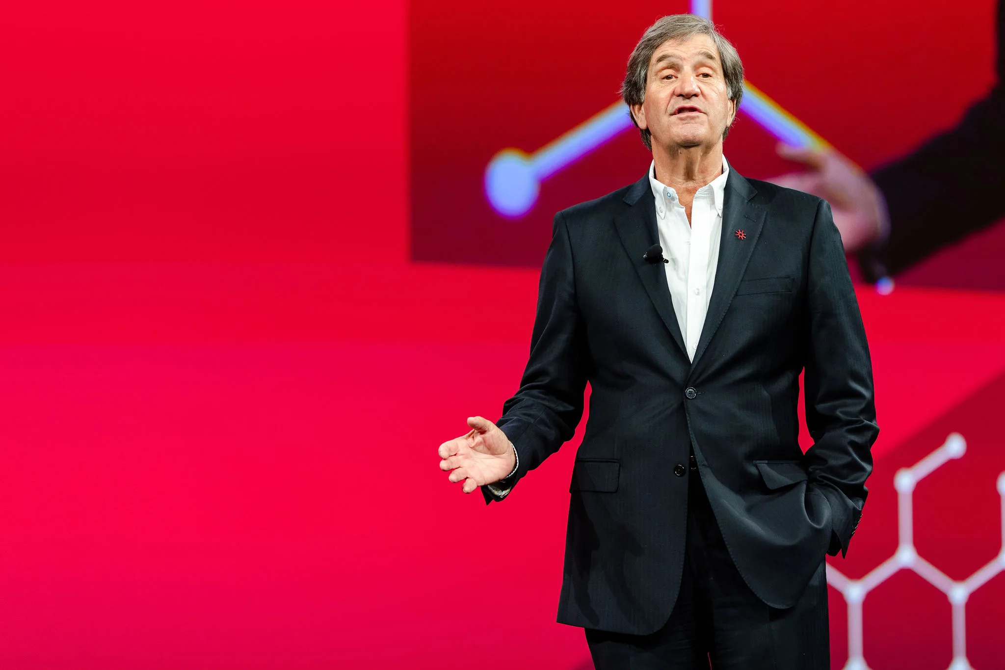 A man in a suit standing in front of a vibrant red background.