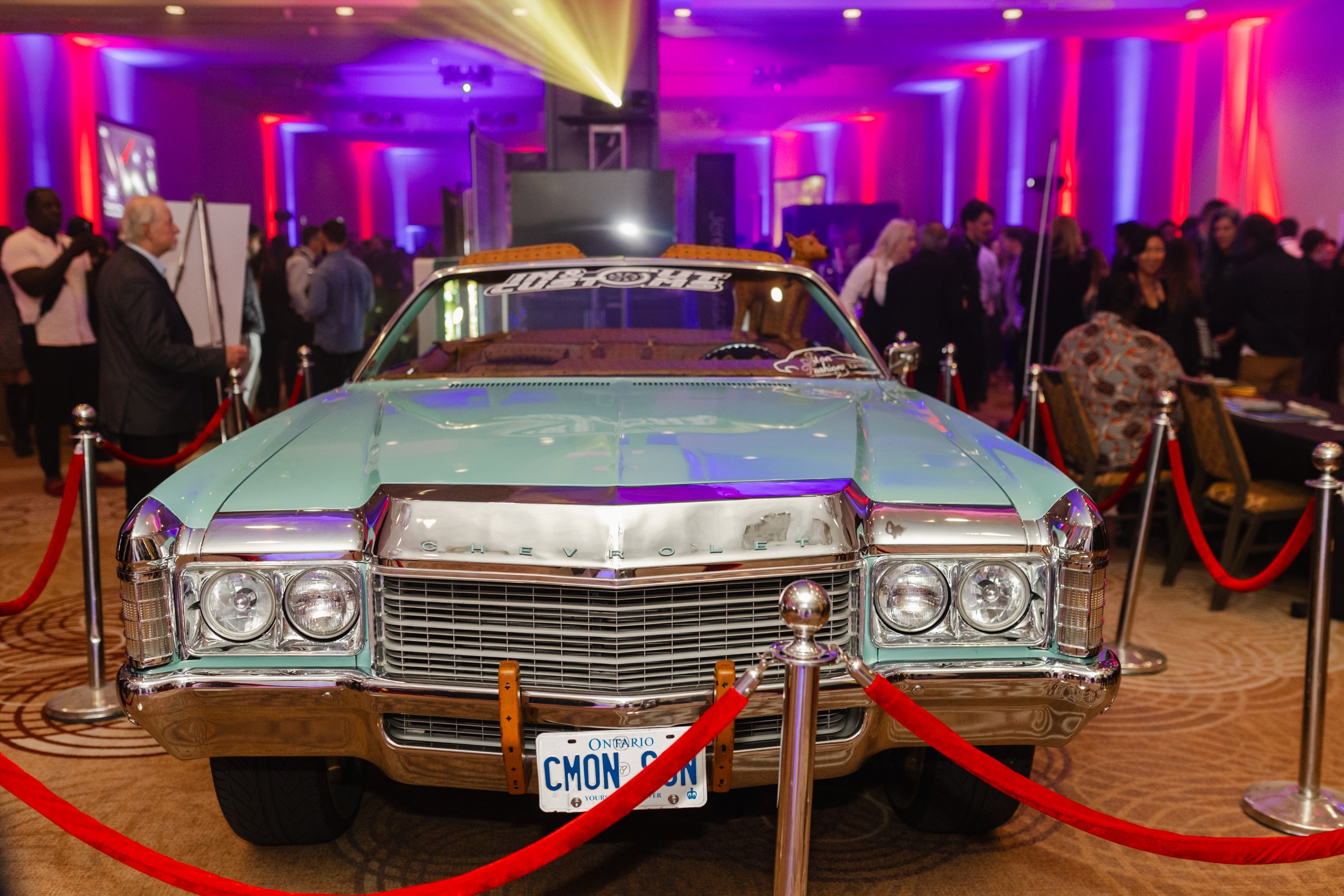 An event photography of a blue Cadillac parked in front of a crowd of people.