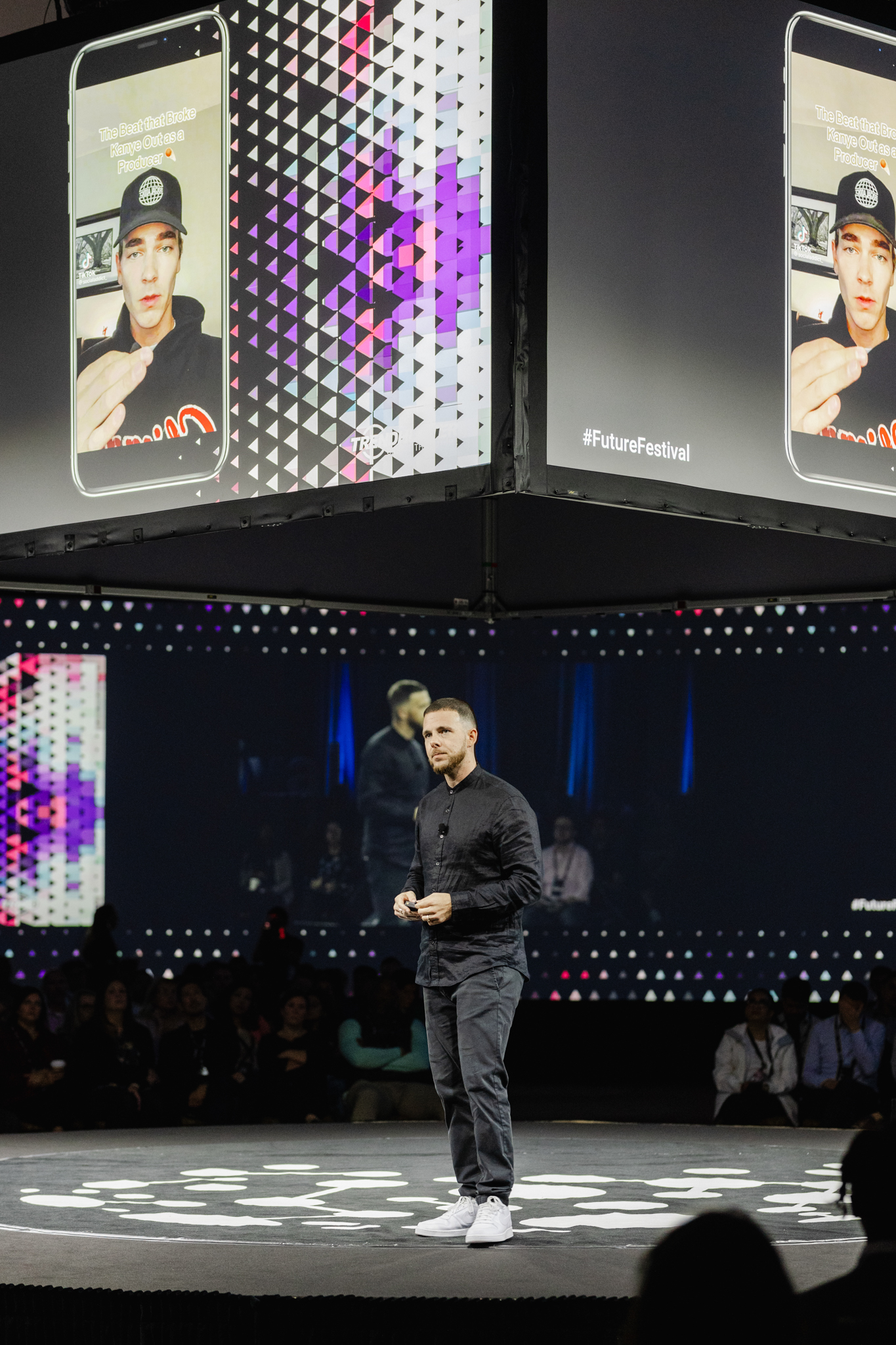 An event photographer captures a man standing on stage in front of a large screen.