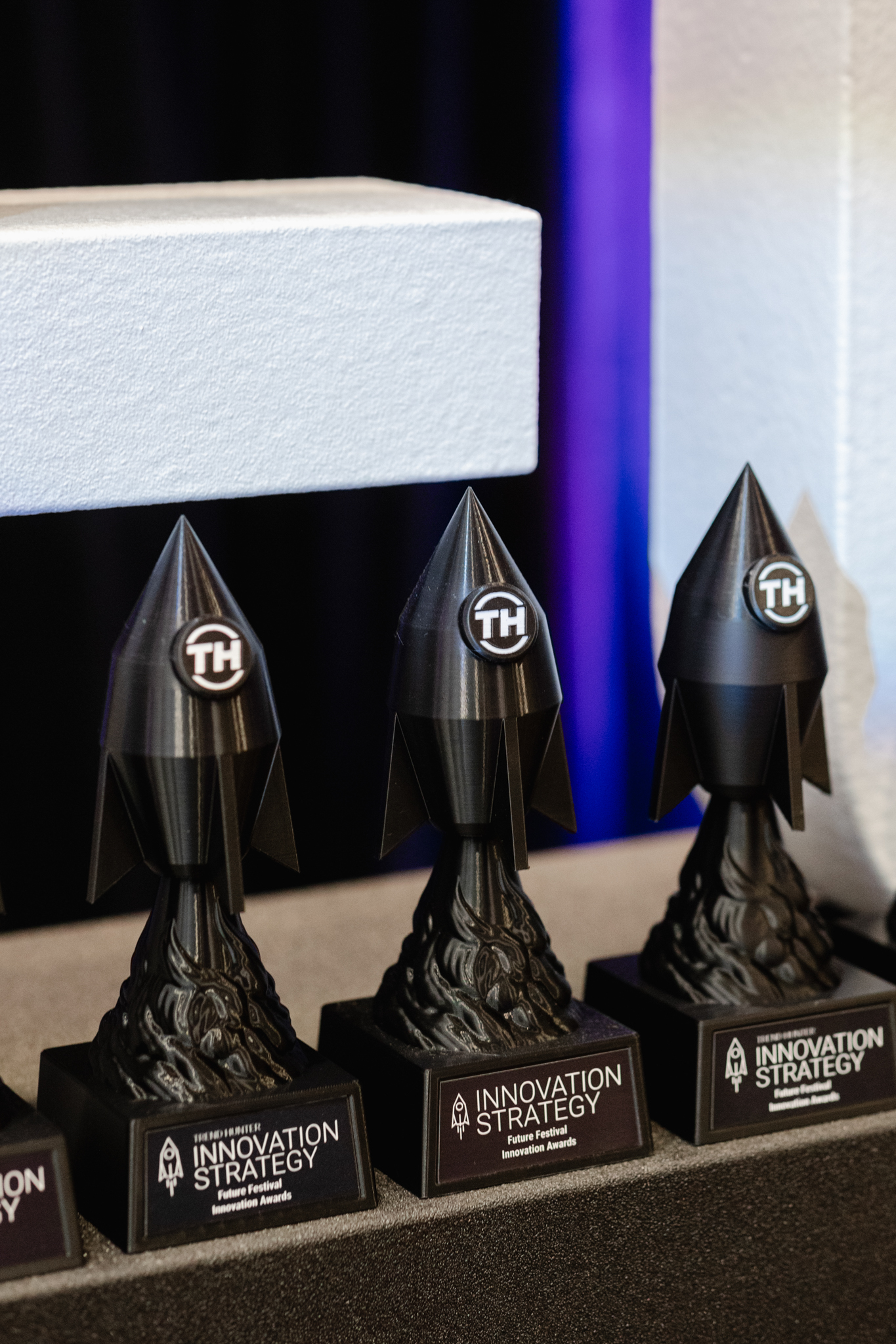Four black trophies displayed on a table during an event.