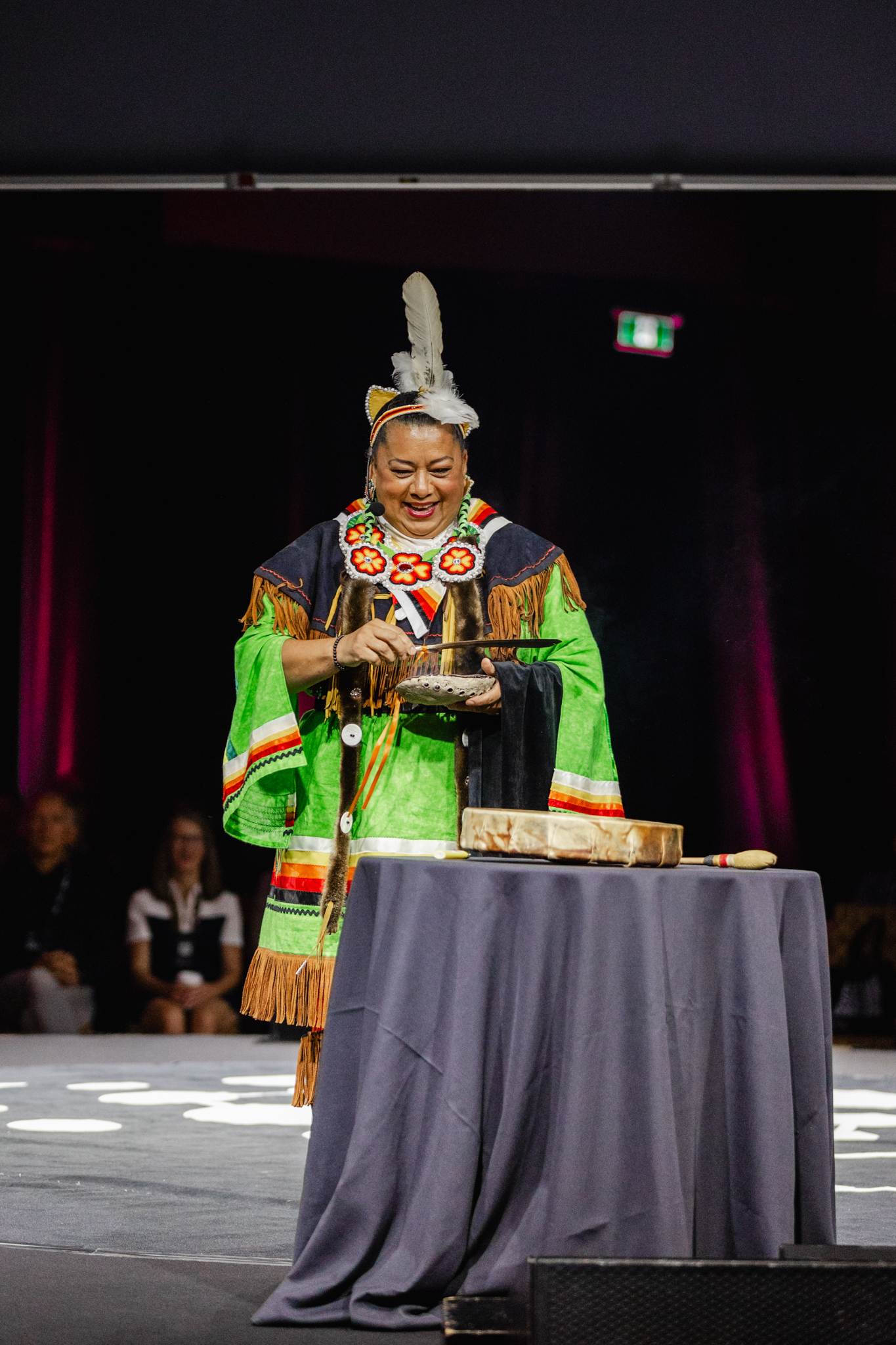 A man in a native outfit, captured in event photography, standing at a table.