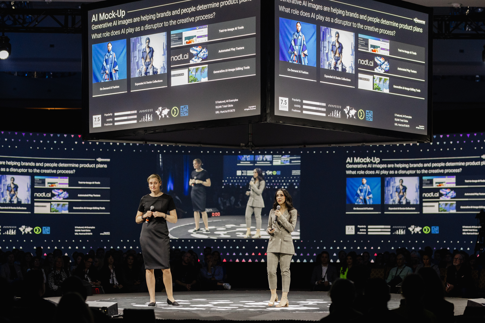 Two women standing on stage in front of a large screen captured in event photography.