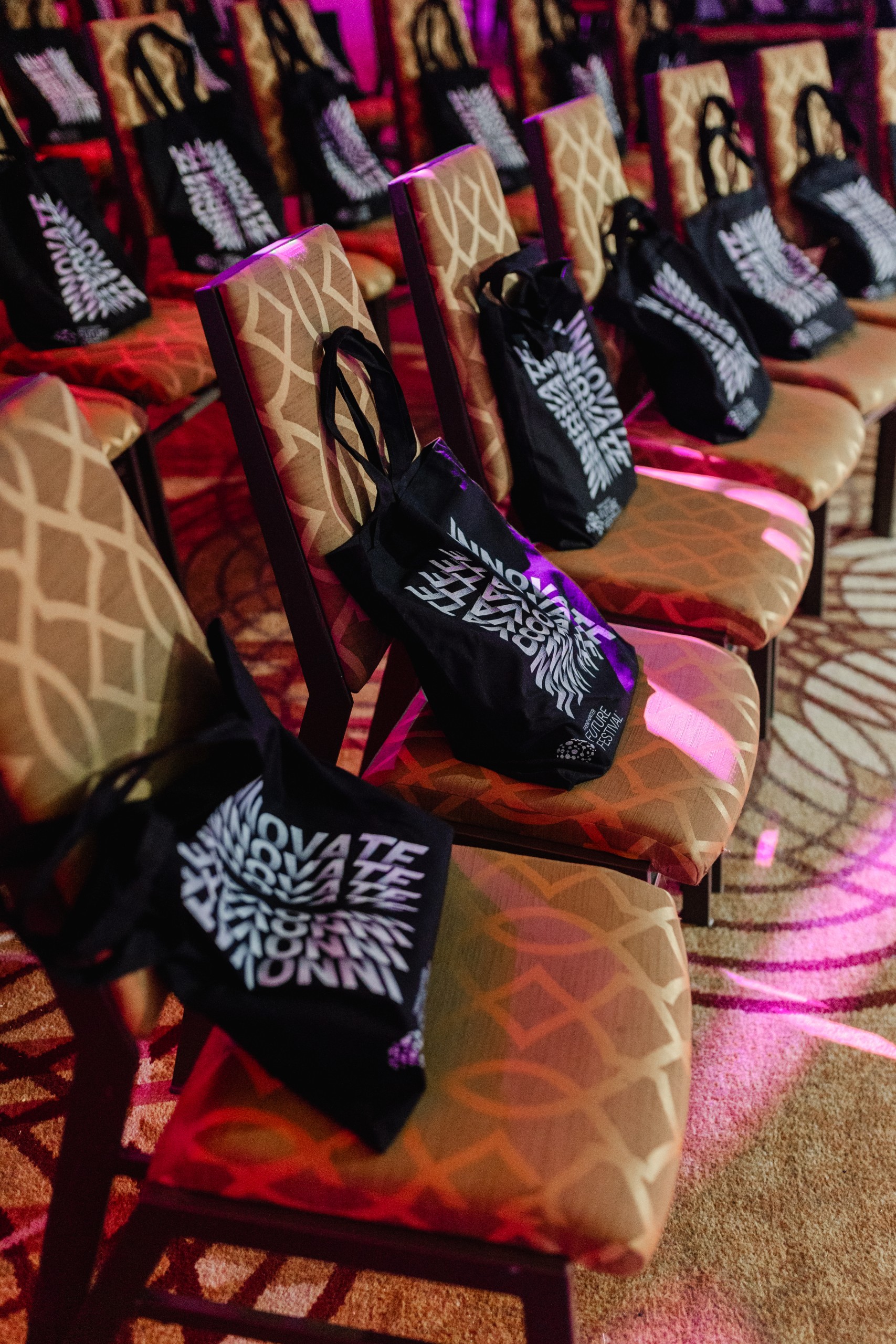 Event photography: A row of chairs with tote bags in front of them, captured through the lens of a photographer documenting the event.