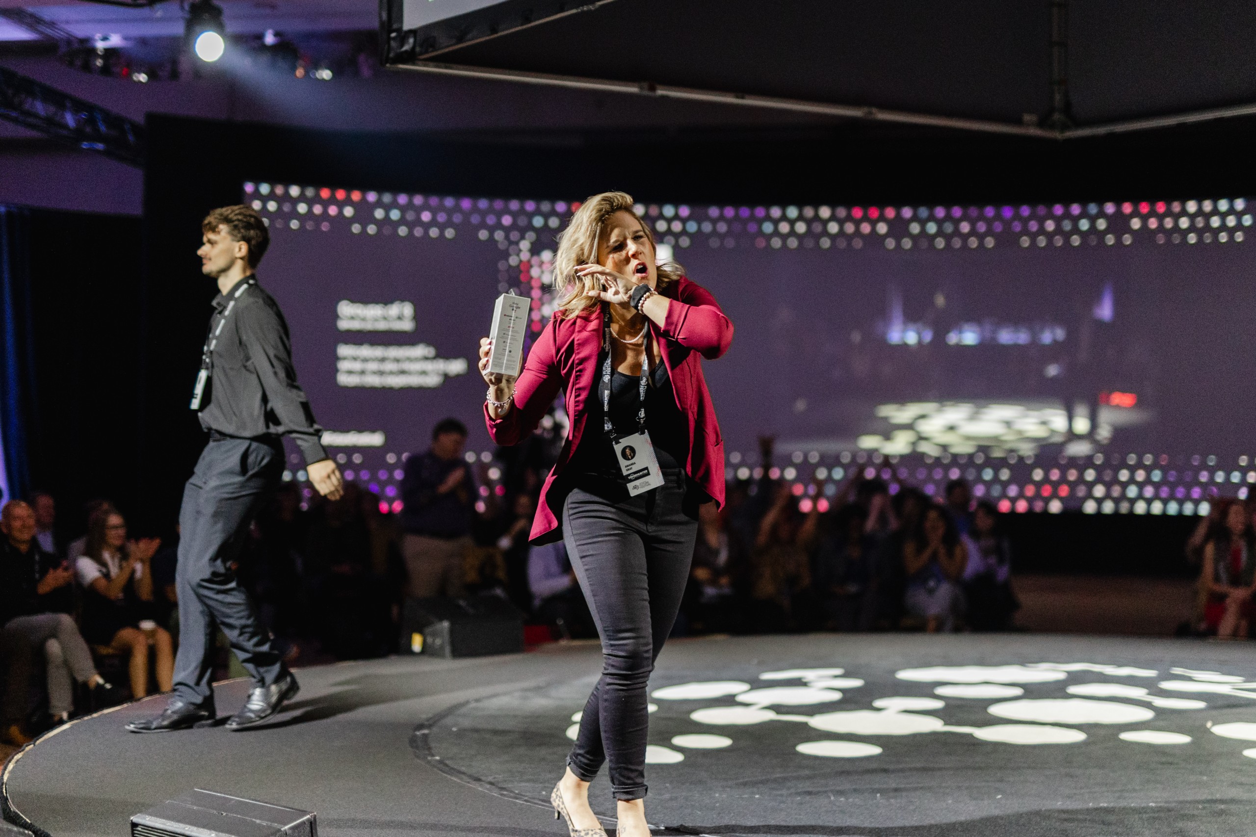 A woman is walking on a runway during an event, with a man in front of her.
