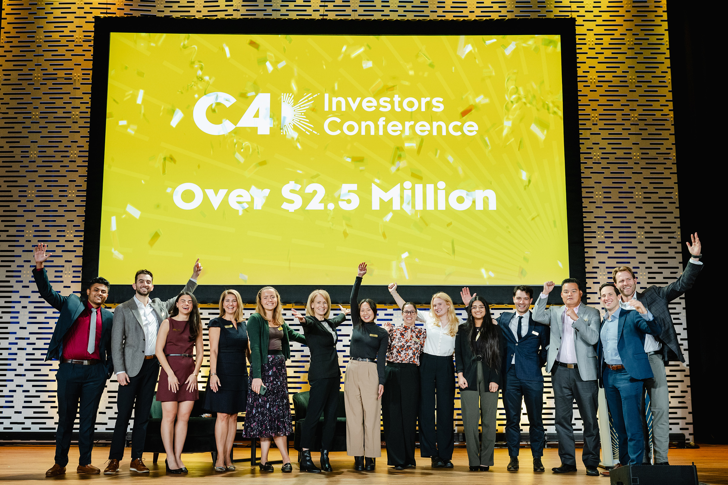 A group of people standing on a stage with the words c4 investors conference over $ 3 million.