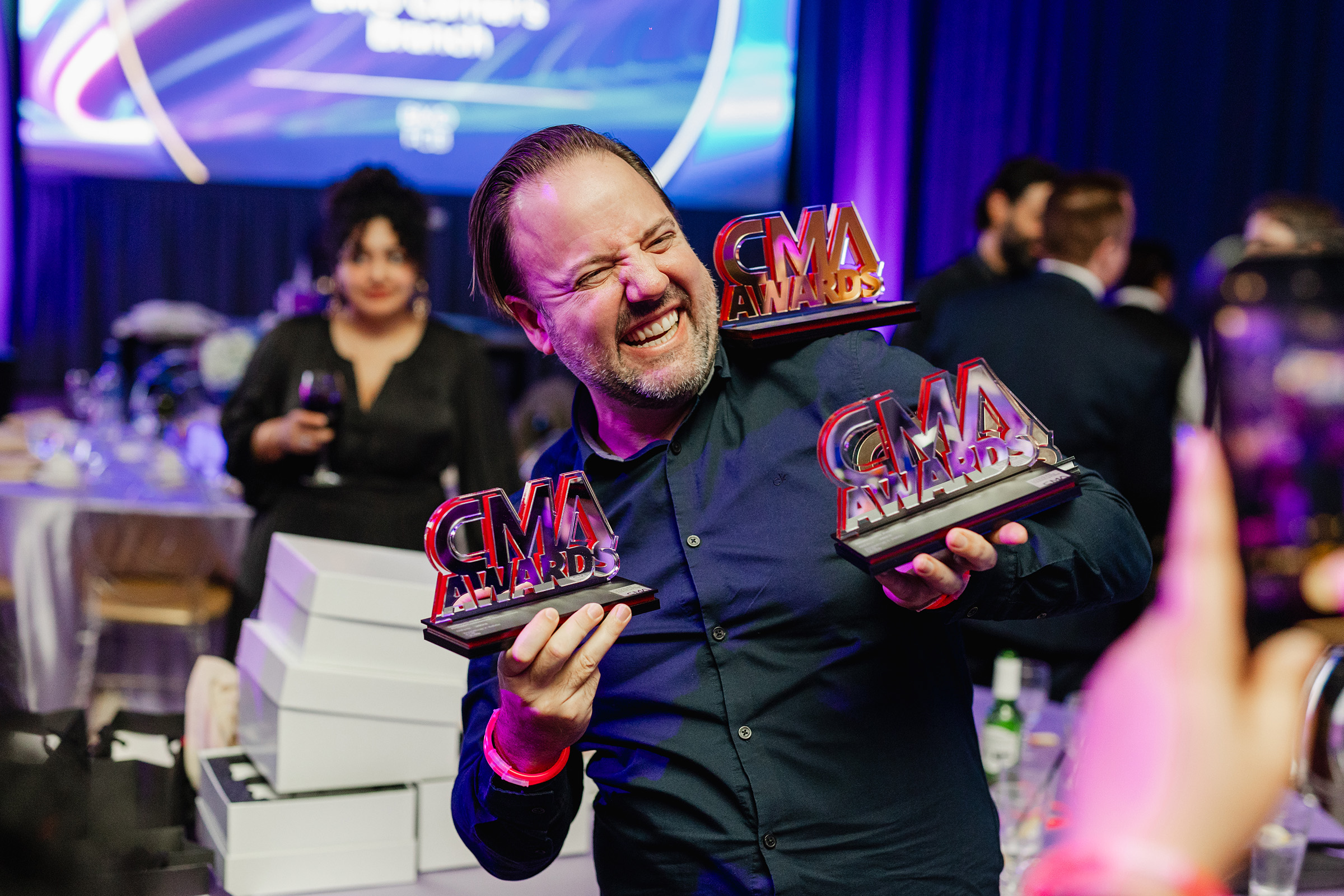 A man showcasing his impressive content creation while proudly holding up two awards at a party.