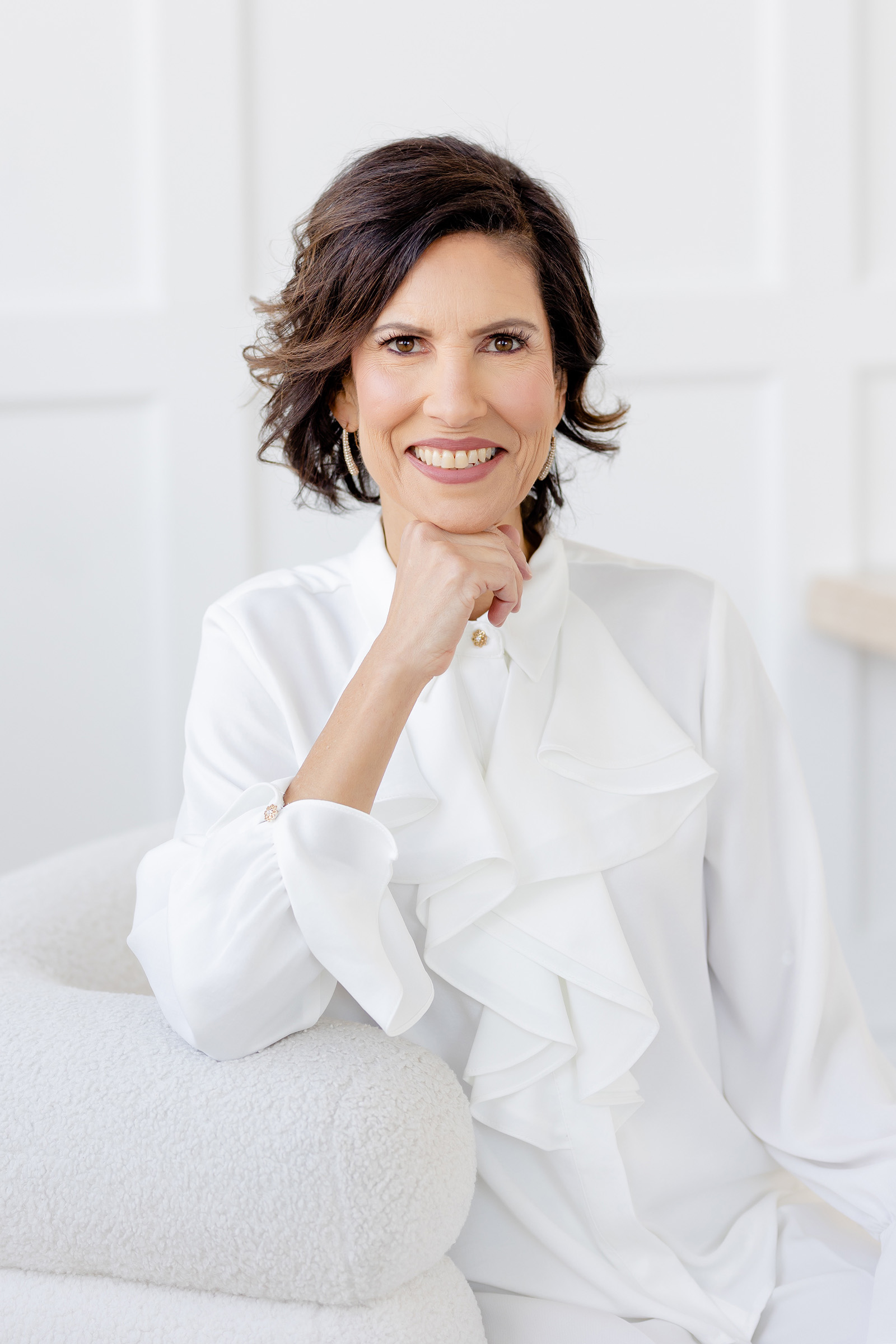 Event photography of a woman in a white shirt elegantly seated on a white couch.