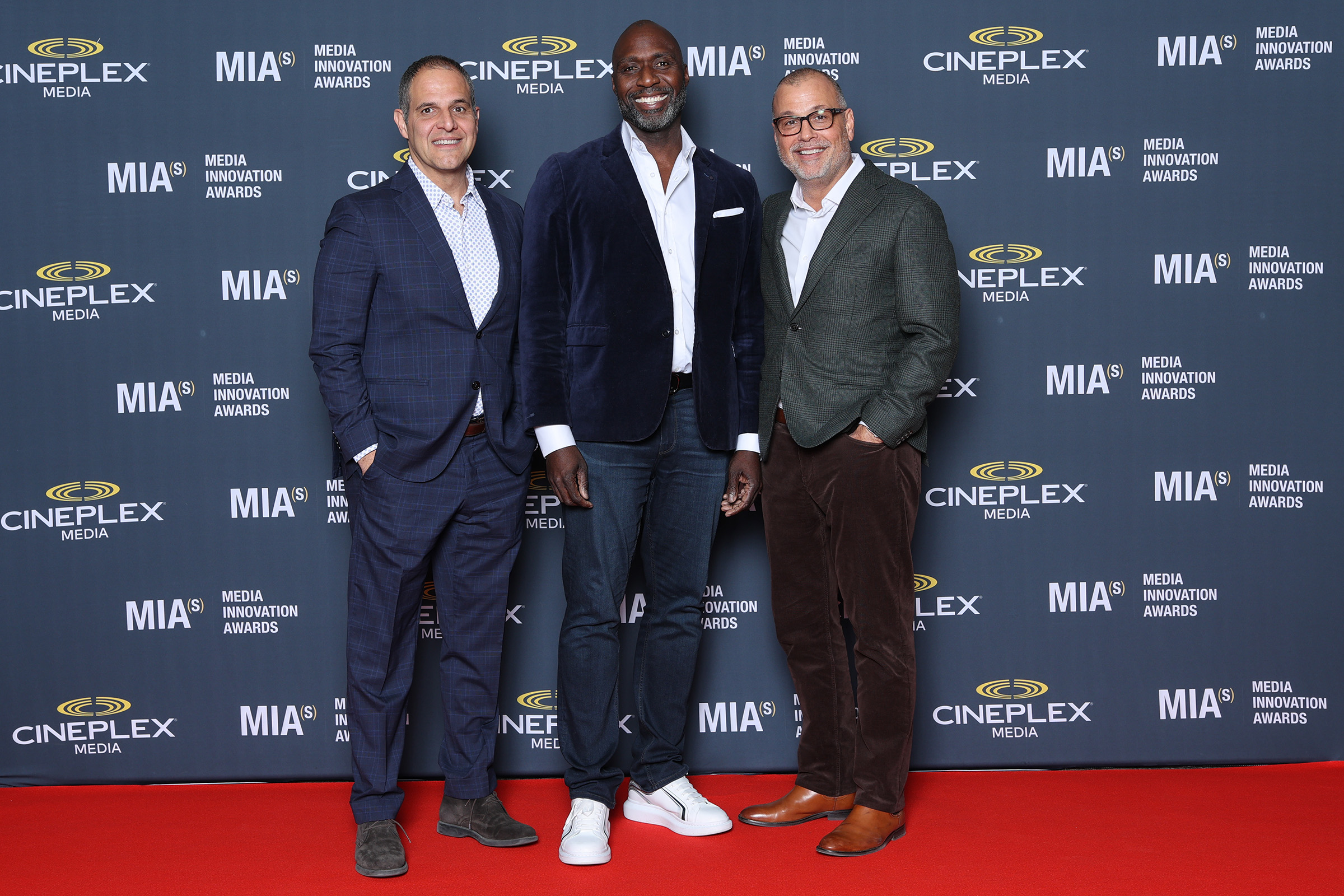 Three men posing for event photography on a red carpet.