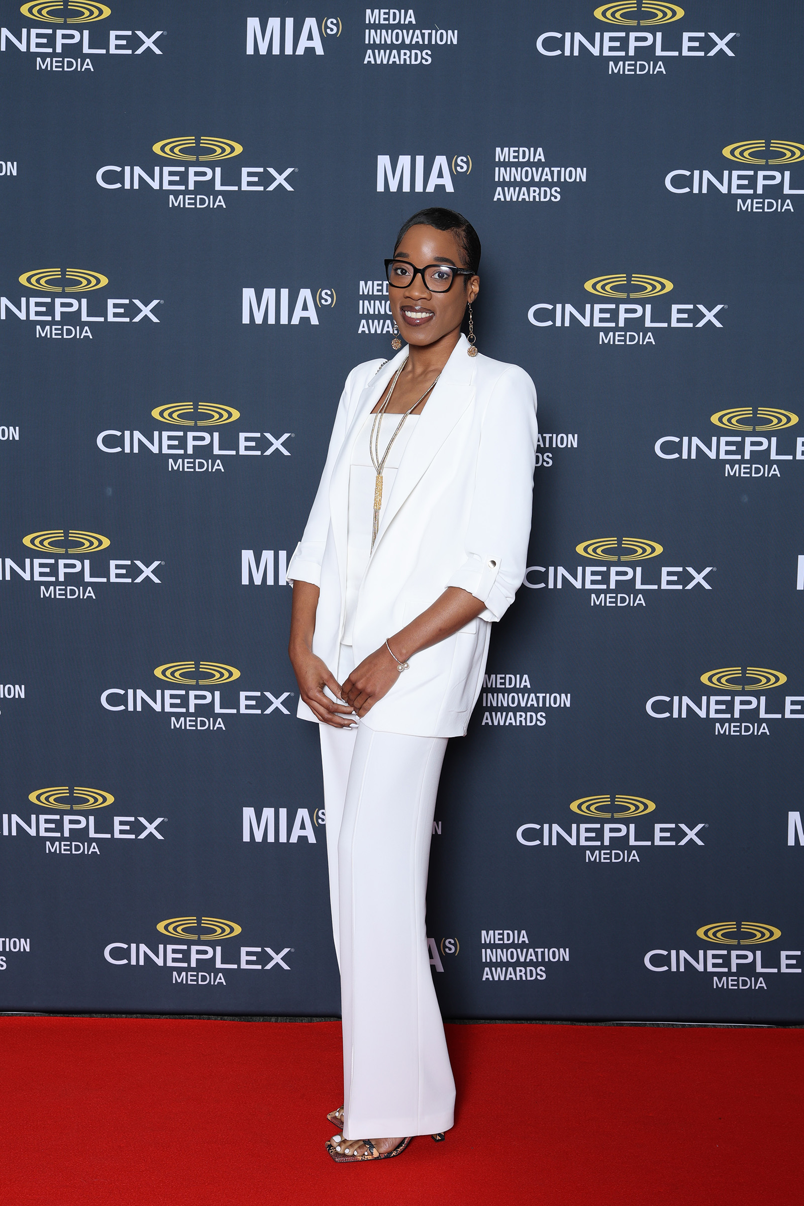 A woman in a white suit gracefully poses on a red carpet, captured through the lens of event photography.