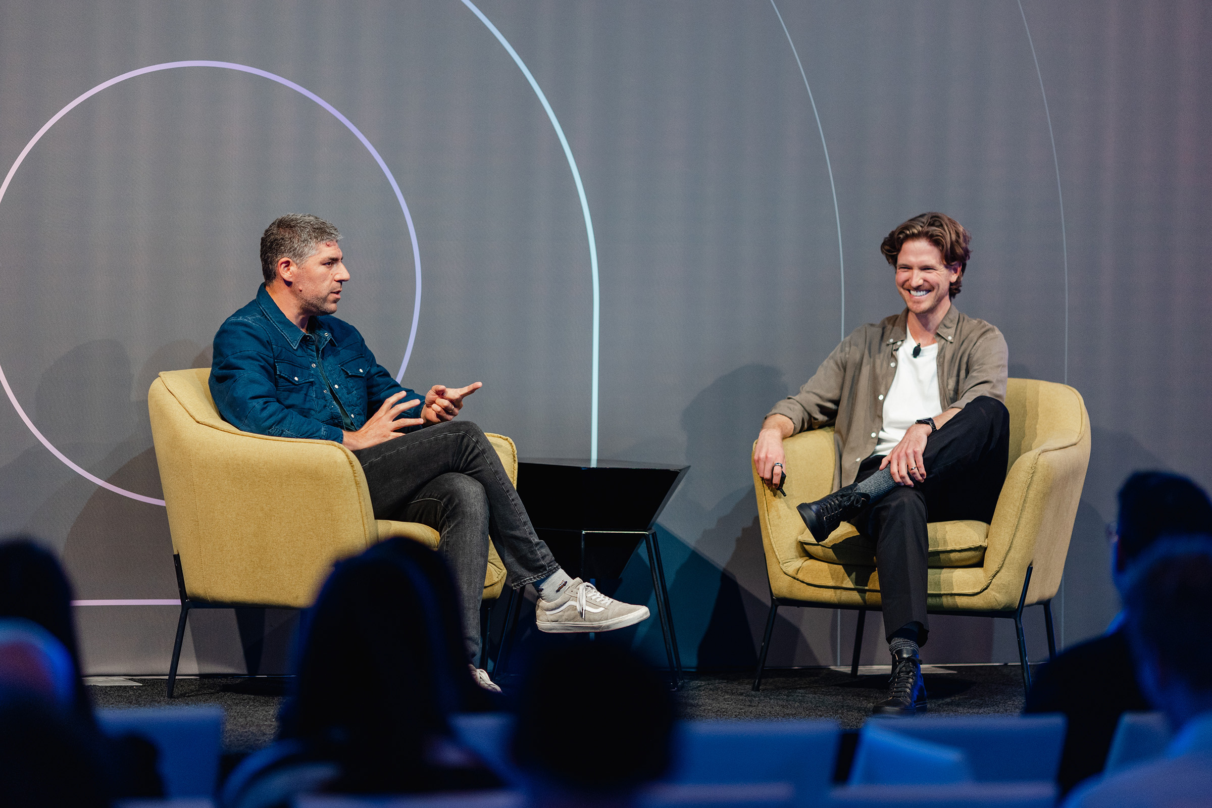 Two men engaged in content creation sit on chairs and engage in a conversation on stage.