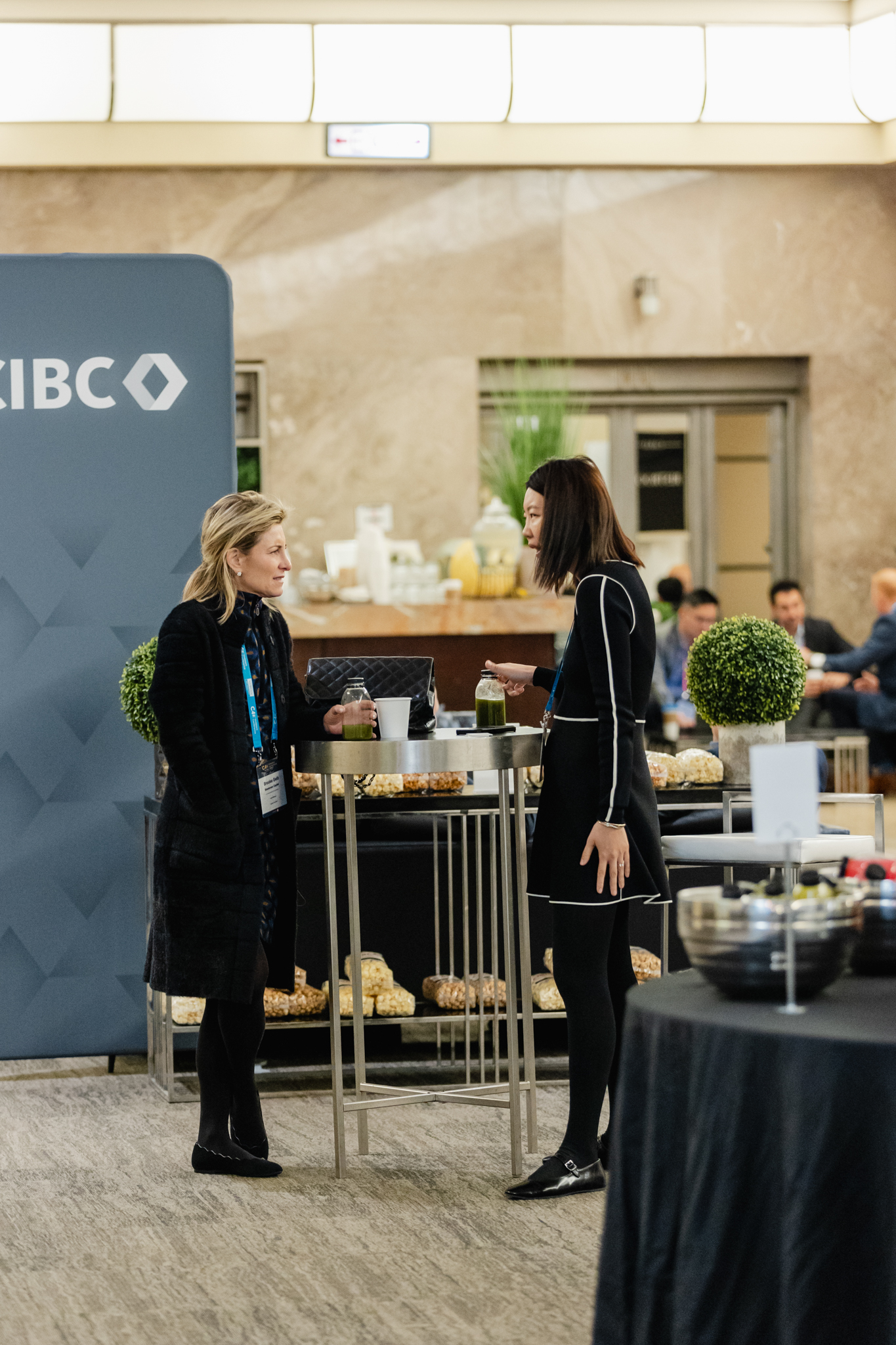 Two women engaging in conversation at a conference event, with an IBC sign prominently displayed.