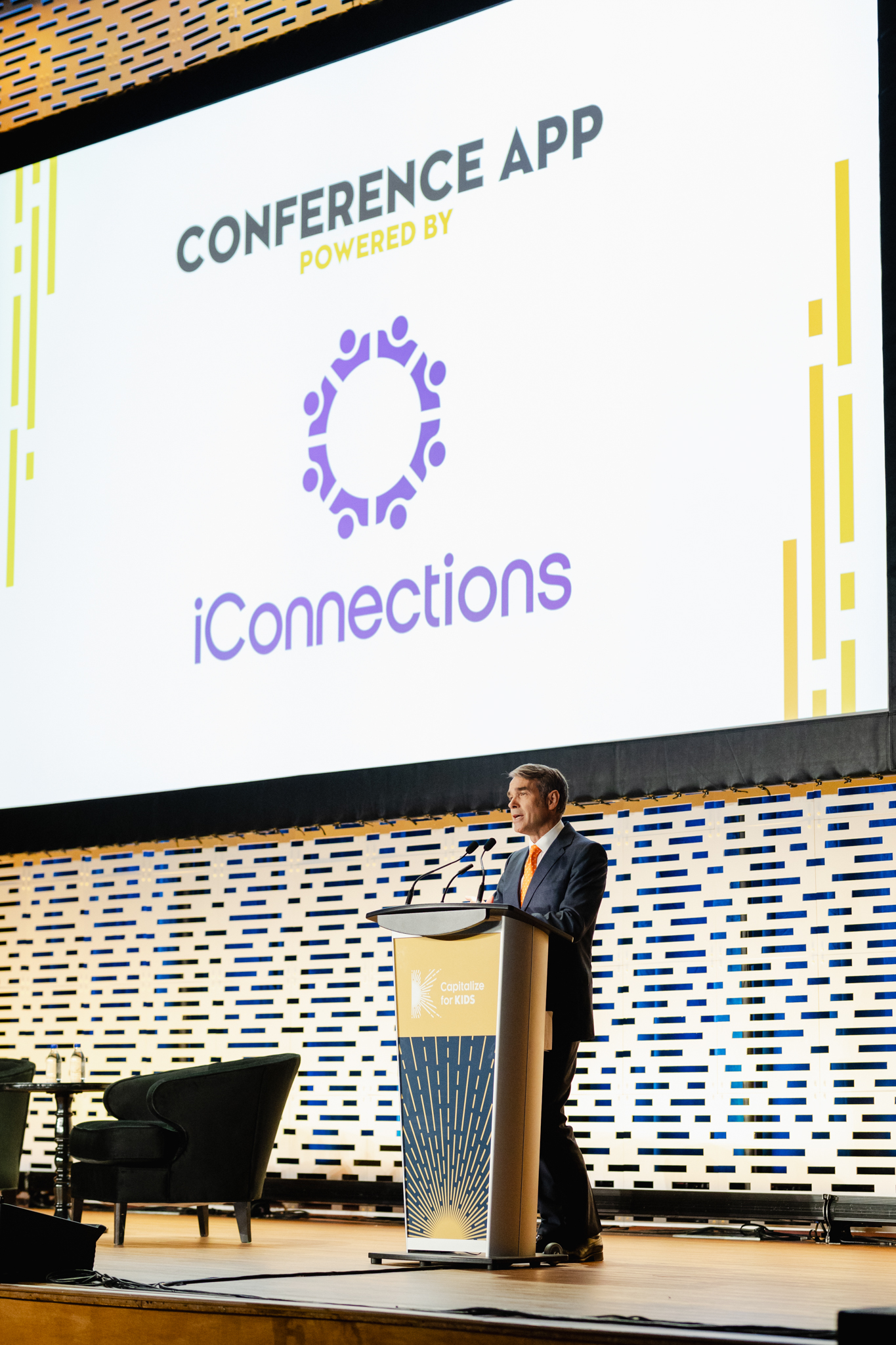 A man standing in front of a screen displaying the words "conference app" for conference photography.