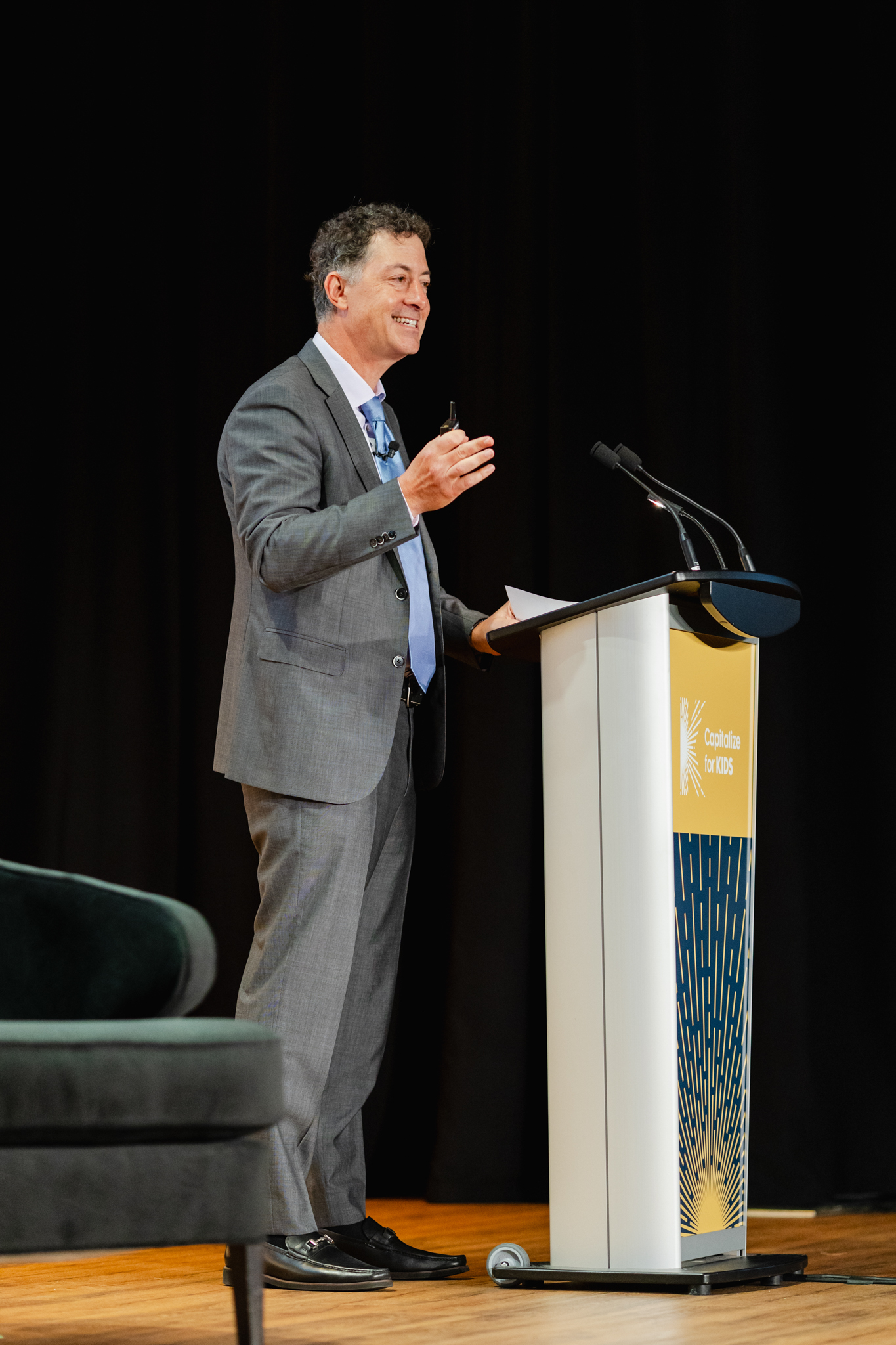 A man in a suit standing at a podium delivering a conference presentation.