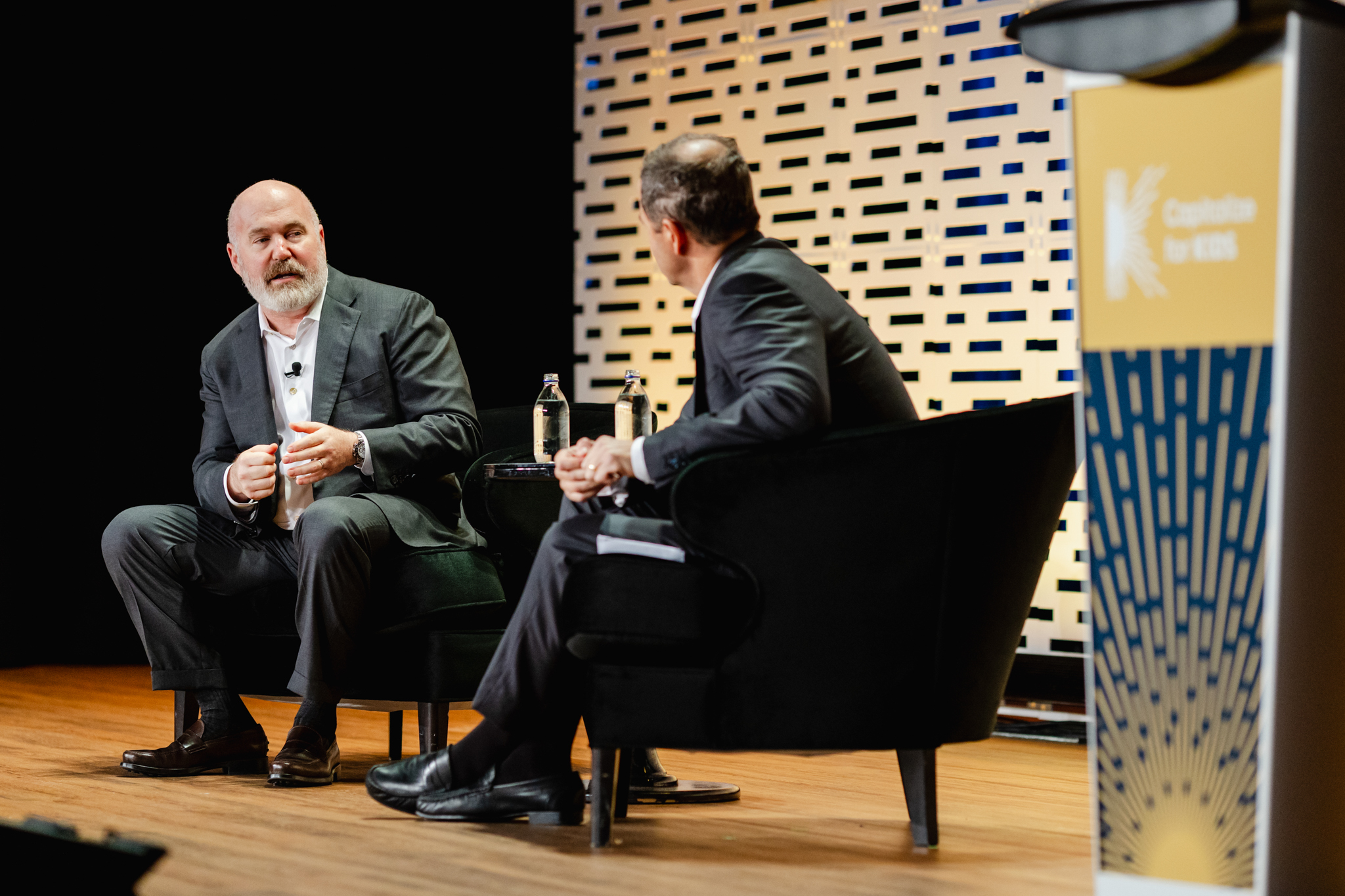 Conference Photography: Two men seated on a stage.