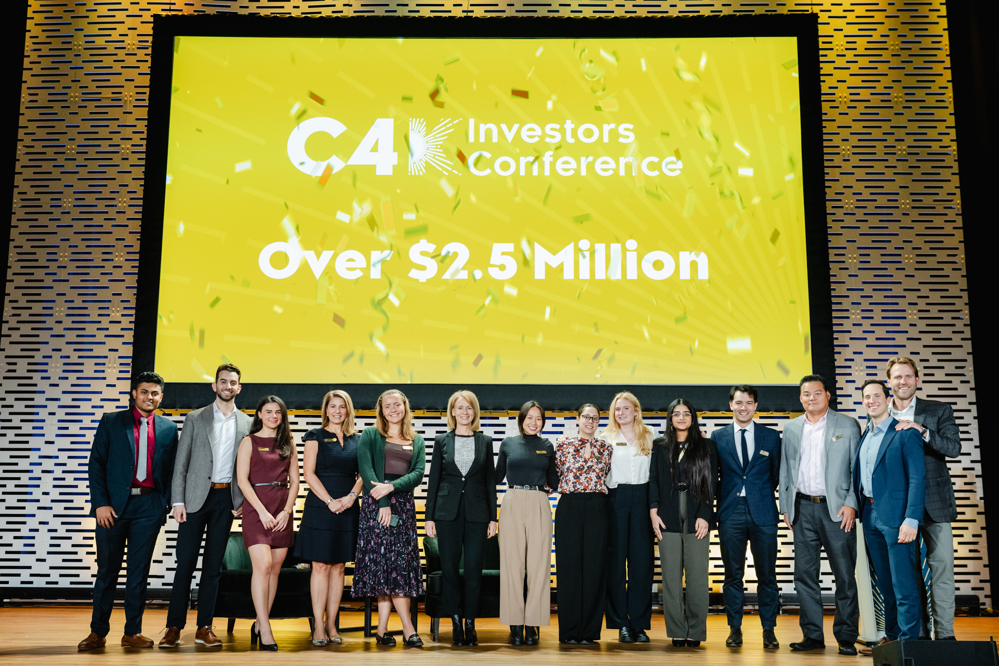 A group of people at a conference, standing in front of a large screen displaying the words "CA Investors Conference" with over $22 million.