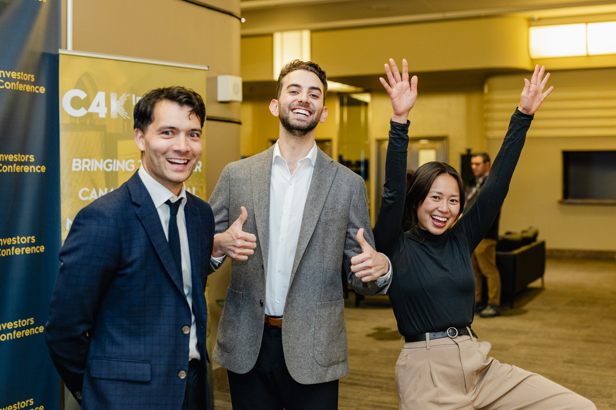 Three people at a conference posing for a photo with thumbs up.
