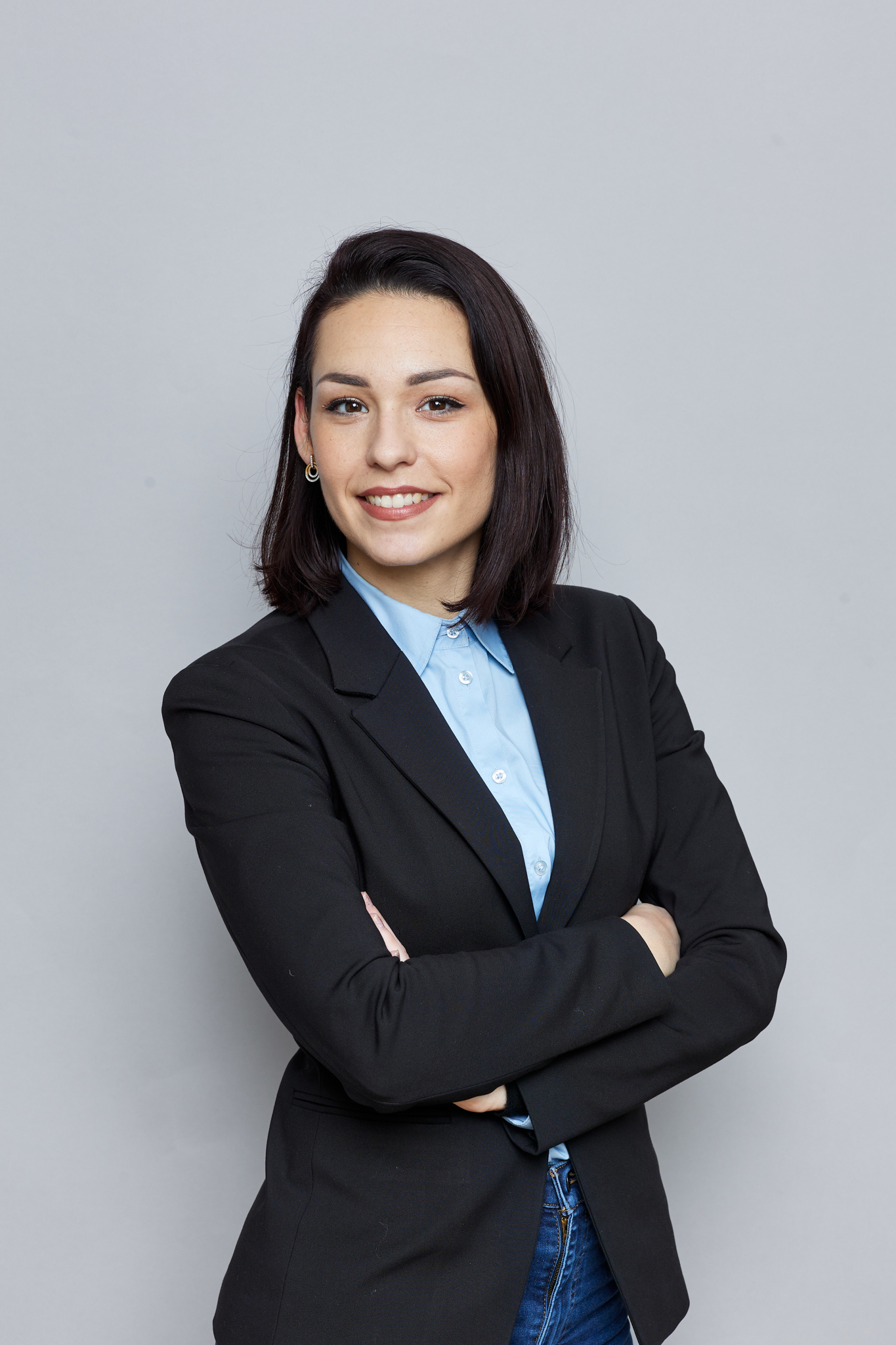 A young business woman posing with her arms crossed on a gray background for event photography.