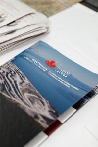 A brochure for invest in Canada on a table with newspapers and event photography in the background.