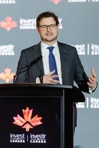Man in a suit speaking at a podium with the Invest Canada logo during an event photography session.