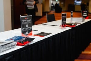 A registration desk with informational signage, pamphlets, and event photography displays, set up for an event.