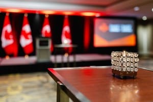 A close-up of a crystal award on a table with a blurred background of a stage adorned with Canadian flags and an event photography presentation screen.