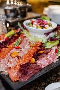 An event photography capture of a charcuterie board featuring an assortment of cured meats and a bowl of salad in the background.