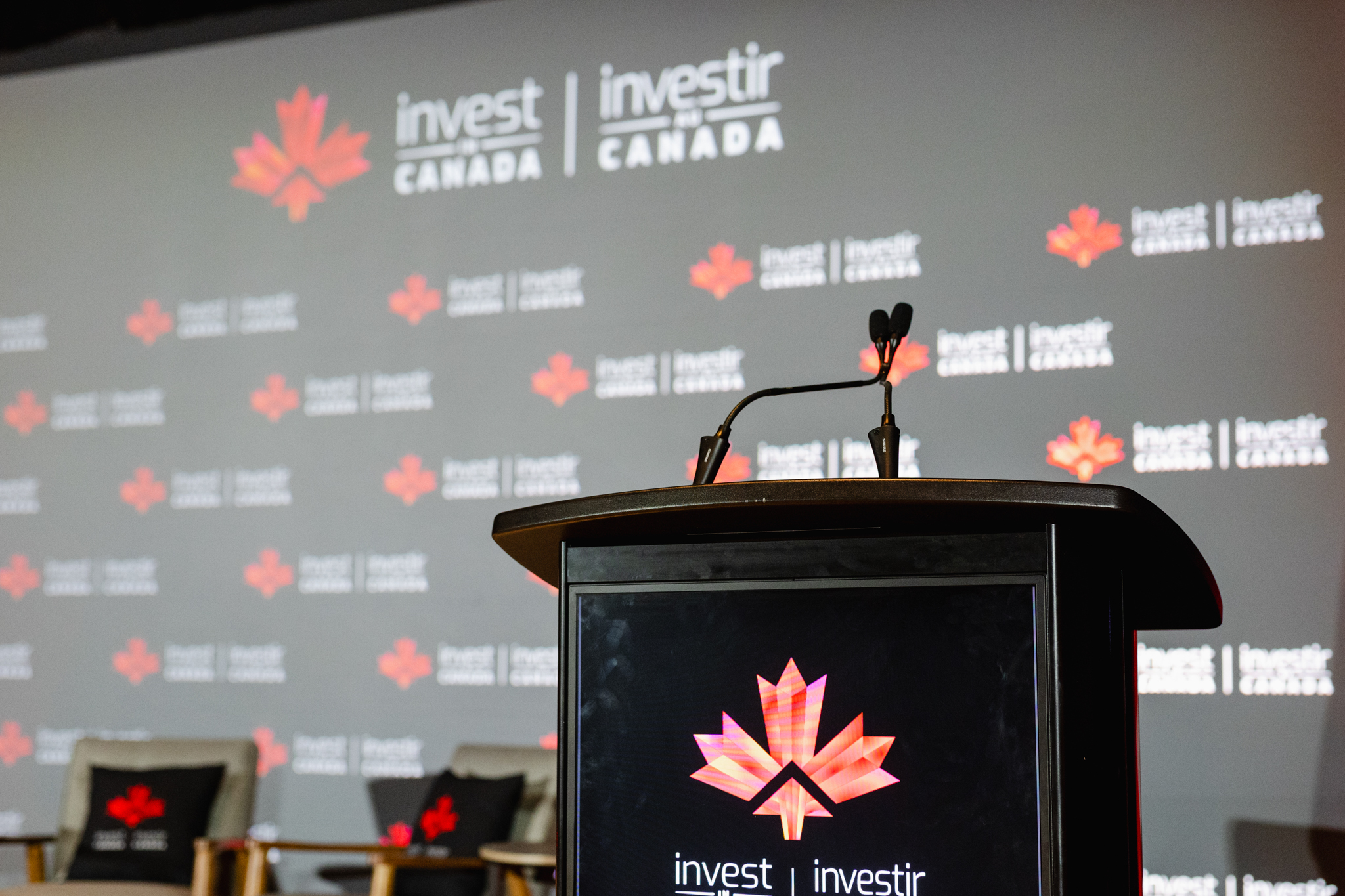 Event photography of a podium with a microphone set against a backdrop featuring multiple "invest in Canada" logos.