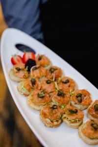 A server presenting a platter of smoked salmon appetizers garnished with herbs and capers, captured in stunning event photography.