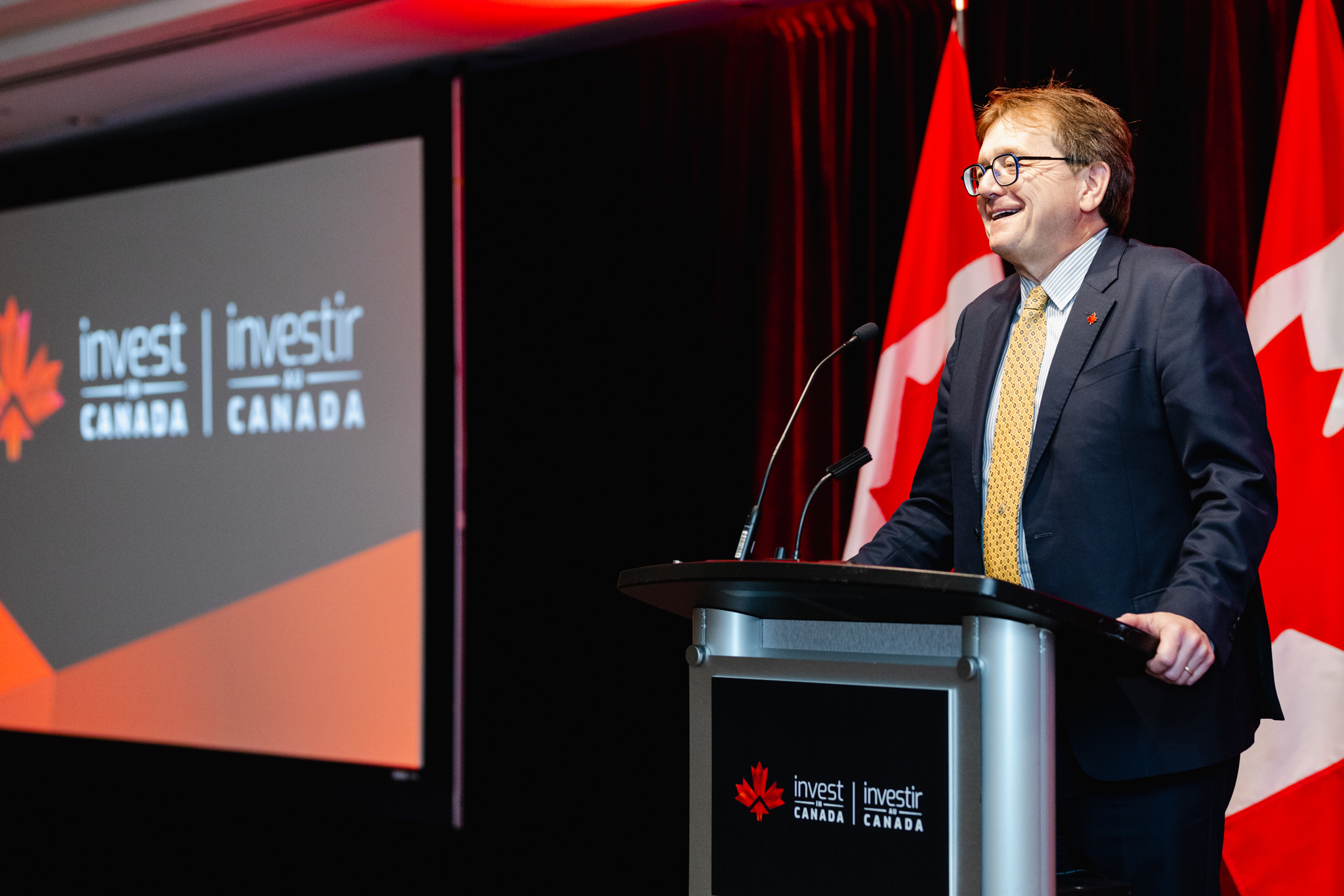 A man speaking at a podium with the "Invest in Canada" logo displayed in the background during an event photography session.