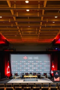 Conference hall arranged for an event photography shoot with invest in Canada branding, empty chairs facing a stage with flags and podiums.