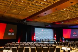 An empty conference room prepared for an event photography session with seating, a stage, and banners for Invest in Canada.