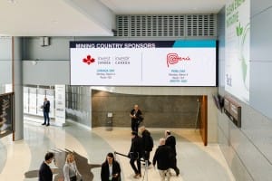A group of people walking in a lobby with banners displaying "mining country sponsors" and information about Canada and Peru investment events, captured in striking event photography.