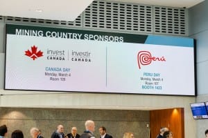 Digital signage displaying information about 'mining country sponsors' with logos for "Invest Canada" and "Peru" at a convention center, featured in event photography.